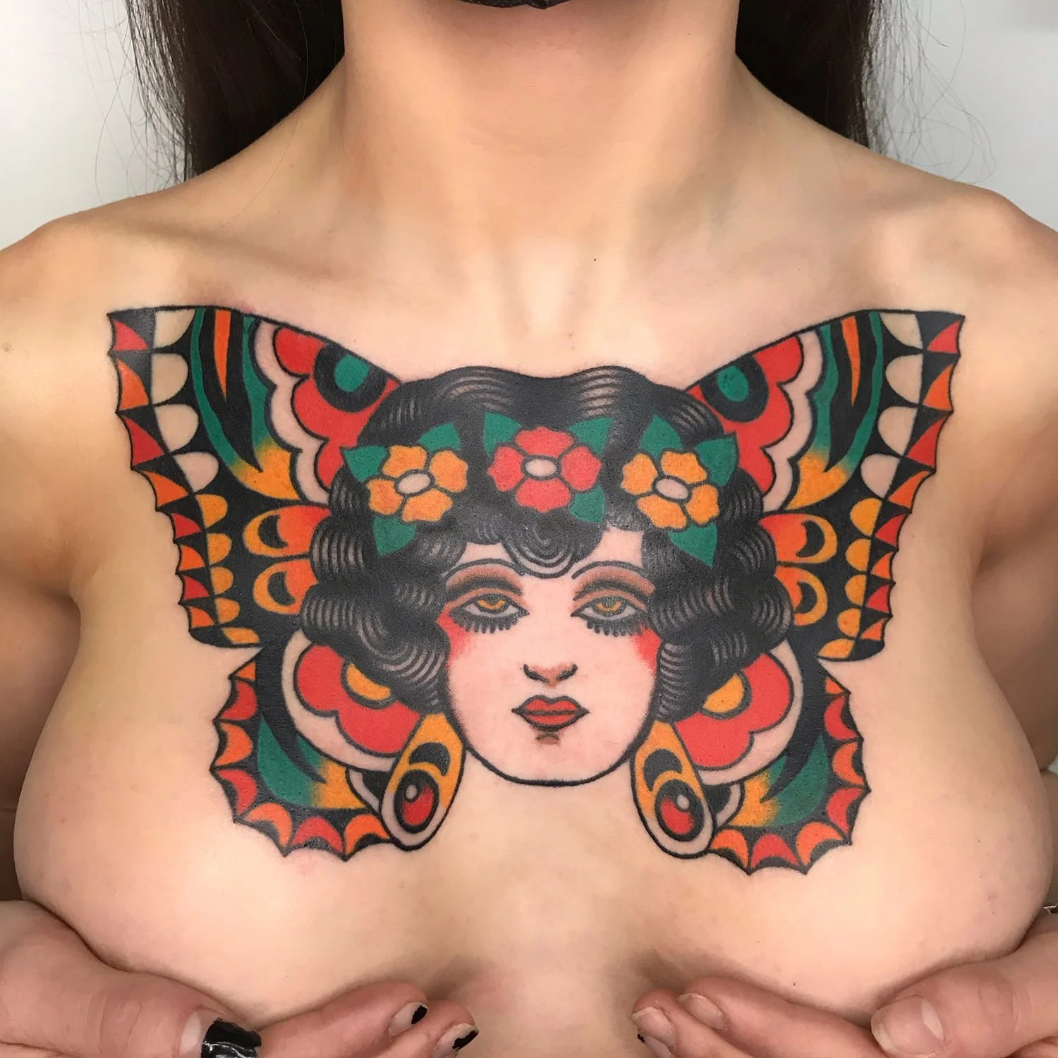 Colorful tattoo on the chest of a woman's face with butterfly wings and floral designs.