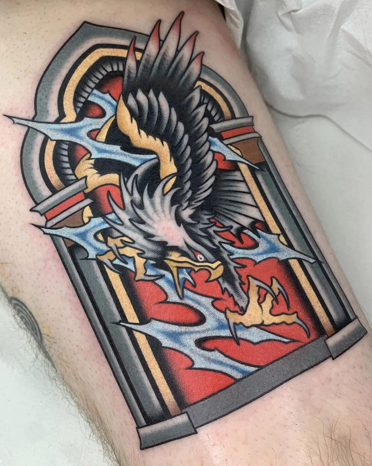 Colorful tattoo of a dragon inside an ornate rectangular frame on skin.