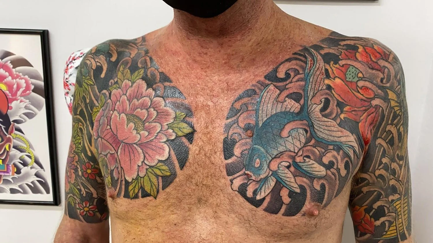 Tattooed man's chest with large pink flower on the left and blue whale on the right, with floral and wave designs on arms and shoulders.