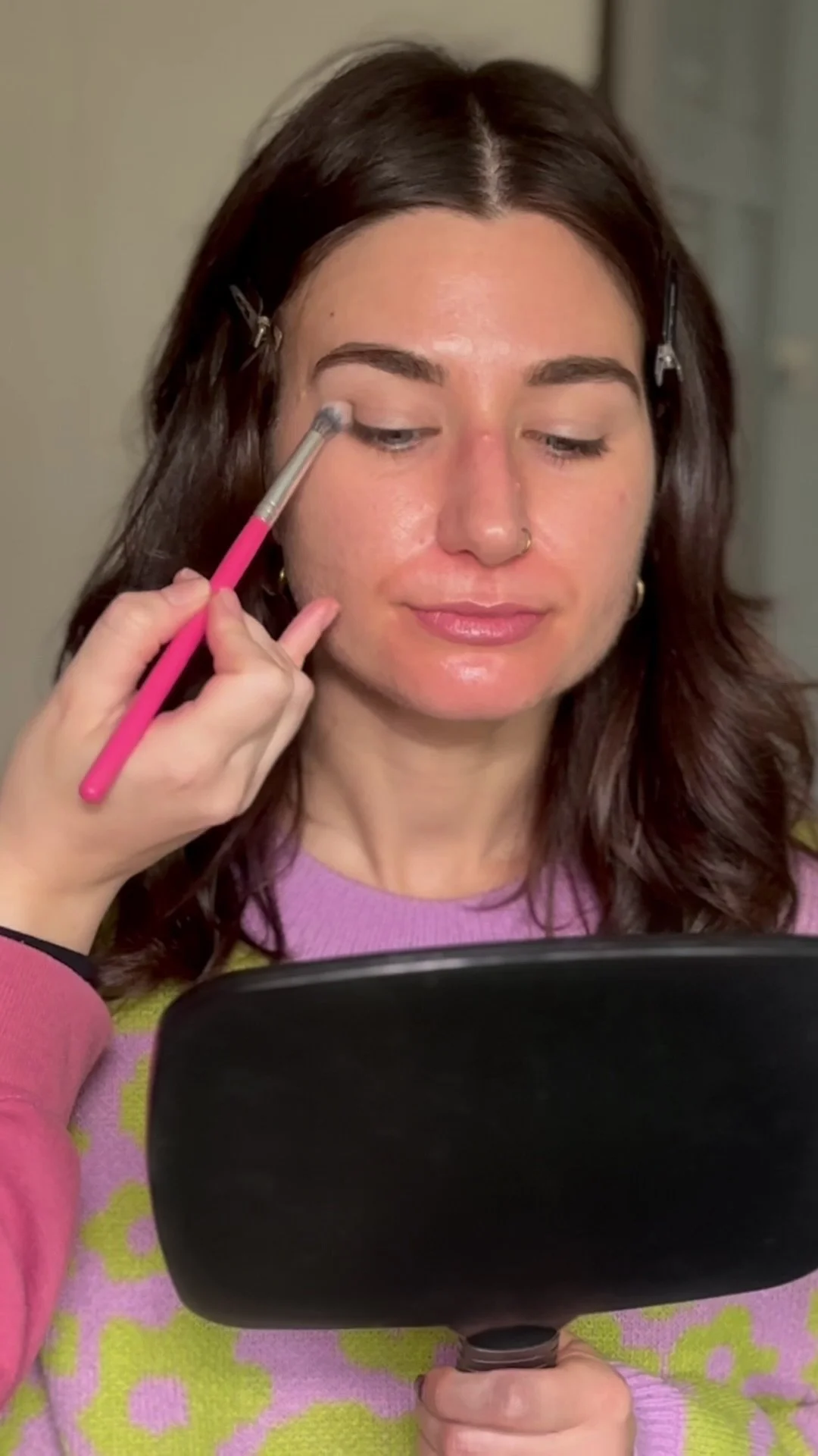A woman looks down in to a mirror as she's shown how and where to apply eyeshadow in a makeup lesson