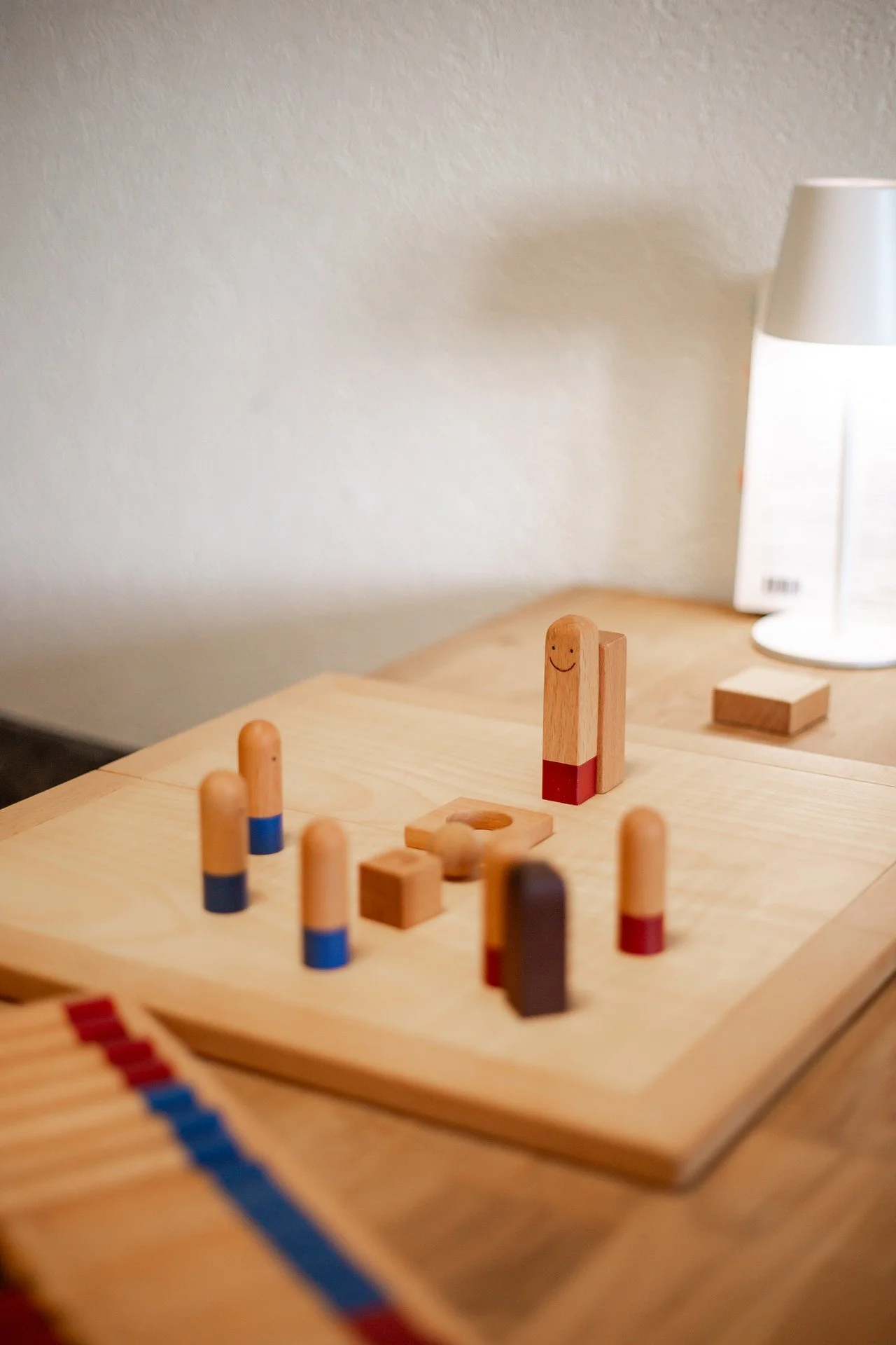 Jeu de société en bois avec plusieurs pièces de différentes formes et couleurs sur une table en bois, éclairée par une lampe blanche.