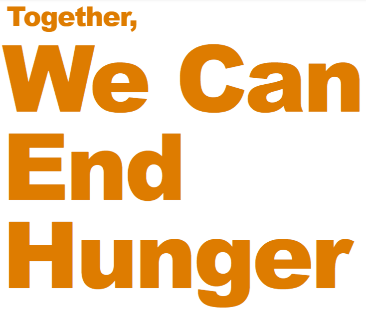 A woman wearing a large sun hat and a blue shirt standing in a greenhouse holding leafy greens.