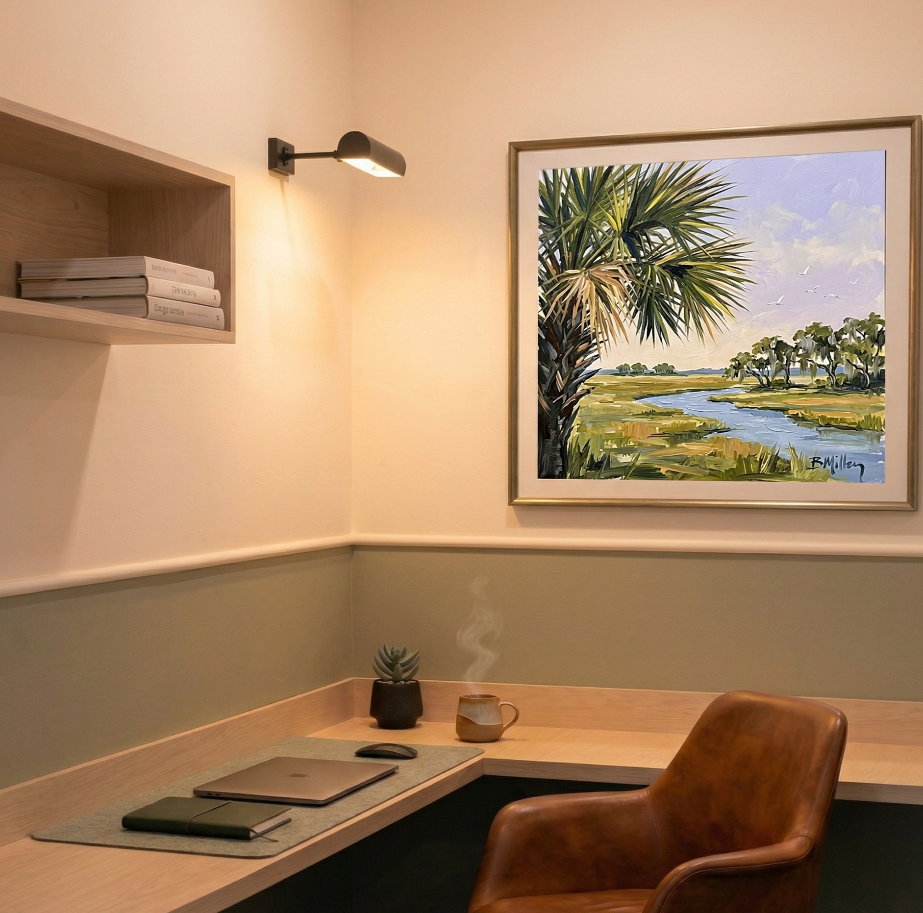 A cozy home office with a wooden desk, a leather chair, a laptop, a notebook, a desk mouse, a potted succulent plant, and a steaming mug. A framed landscape painting of a river and trees hangs on the wall, illuminated by a black wall sconce.