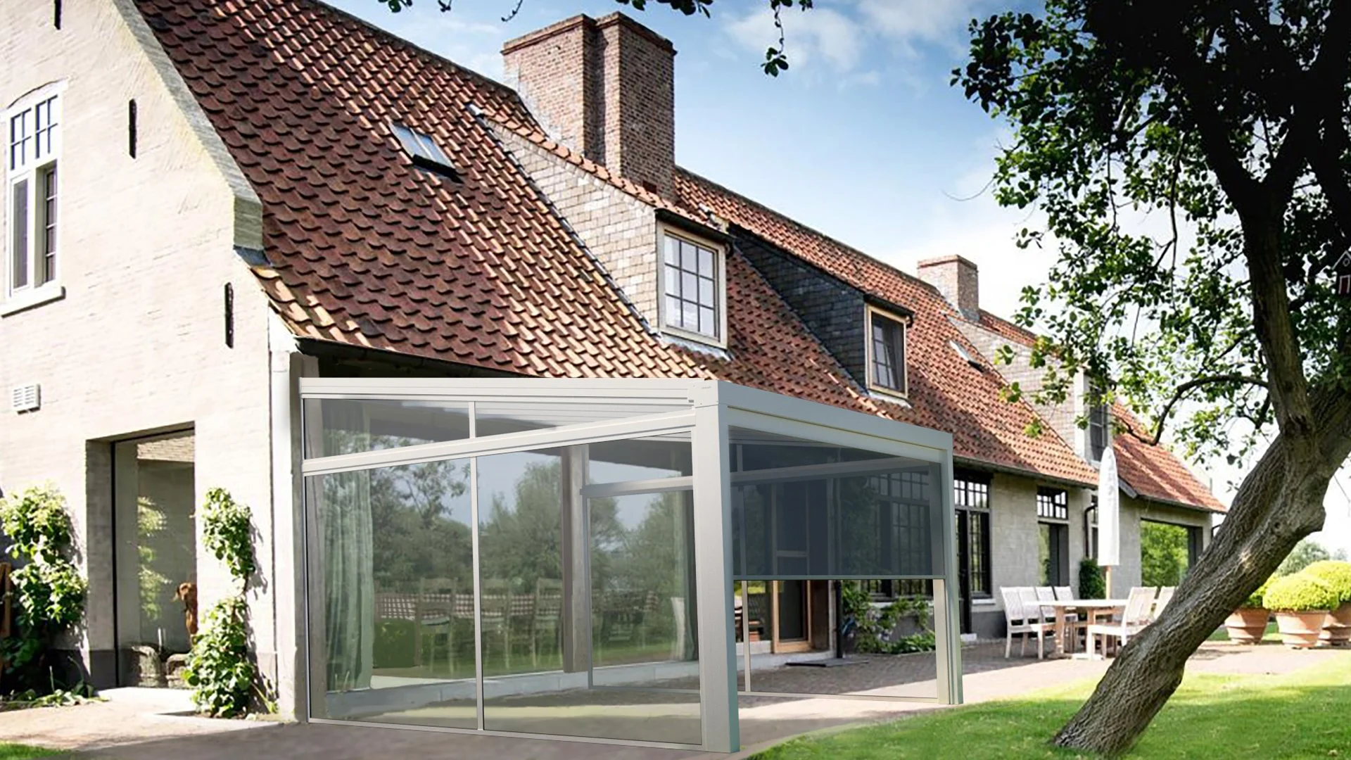 Maison ancienne avec un toit en tuiles rouges, une extension en verre et un jardin avec des arbres, un mobilier de patio et des plantes.