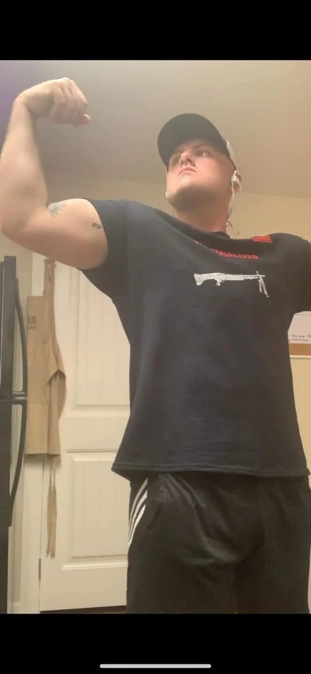 Person wearing a hat and black t-shirt flexing muscles in a room.