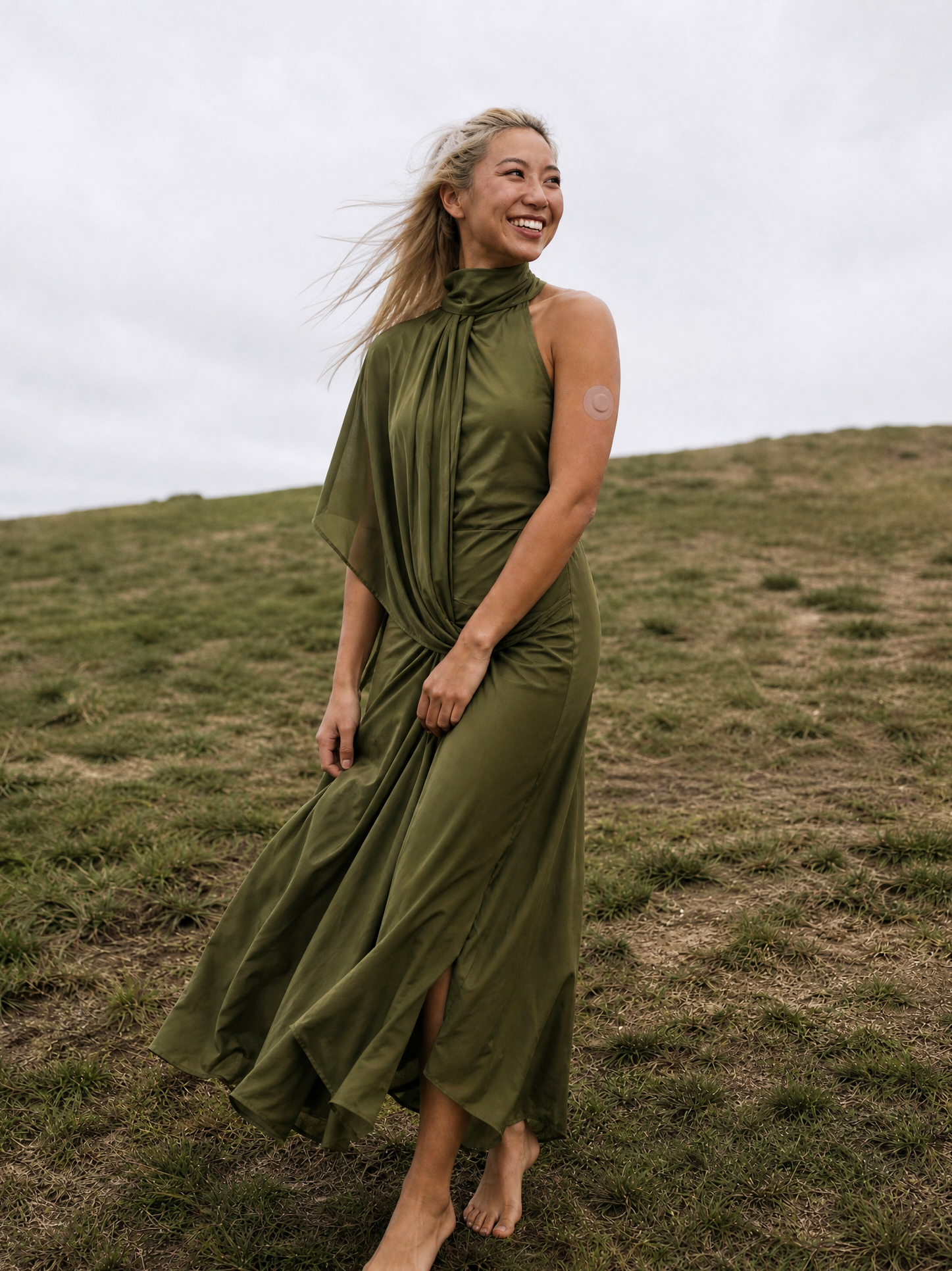 Beautiful Blonde Asian Model in a Dries Van Noten Dress, in the countryside of England, shoeless wearing a skintone overlay patch for a CGM sensor on her arm.