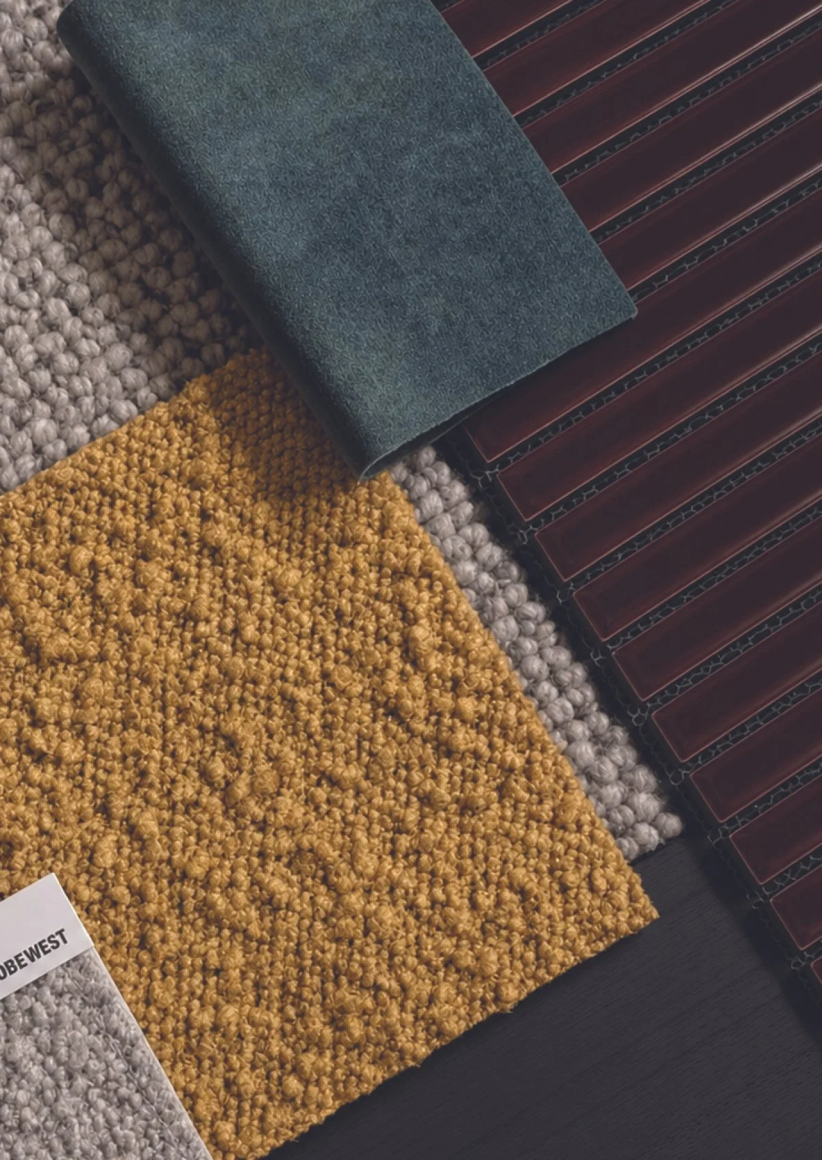 Close-up of various boucle samples with different textures and colors, including yellow, gray, and dark red with black pattern, laid out on a dark surface.