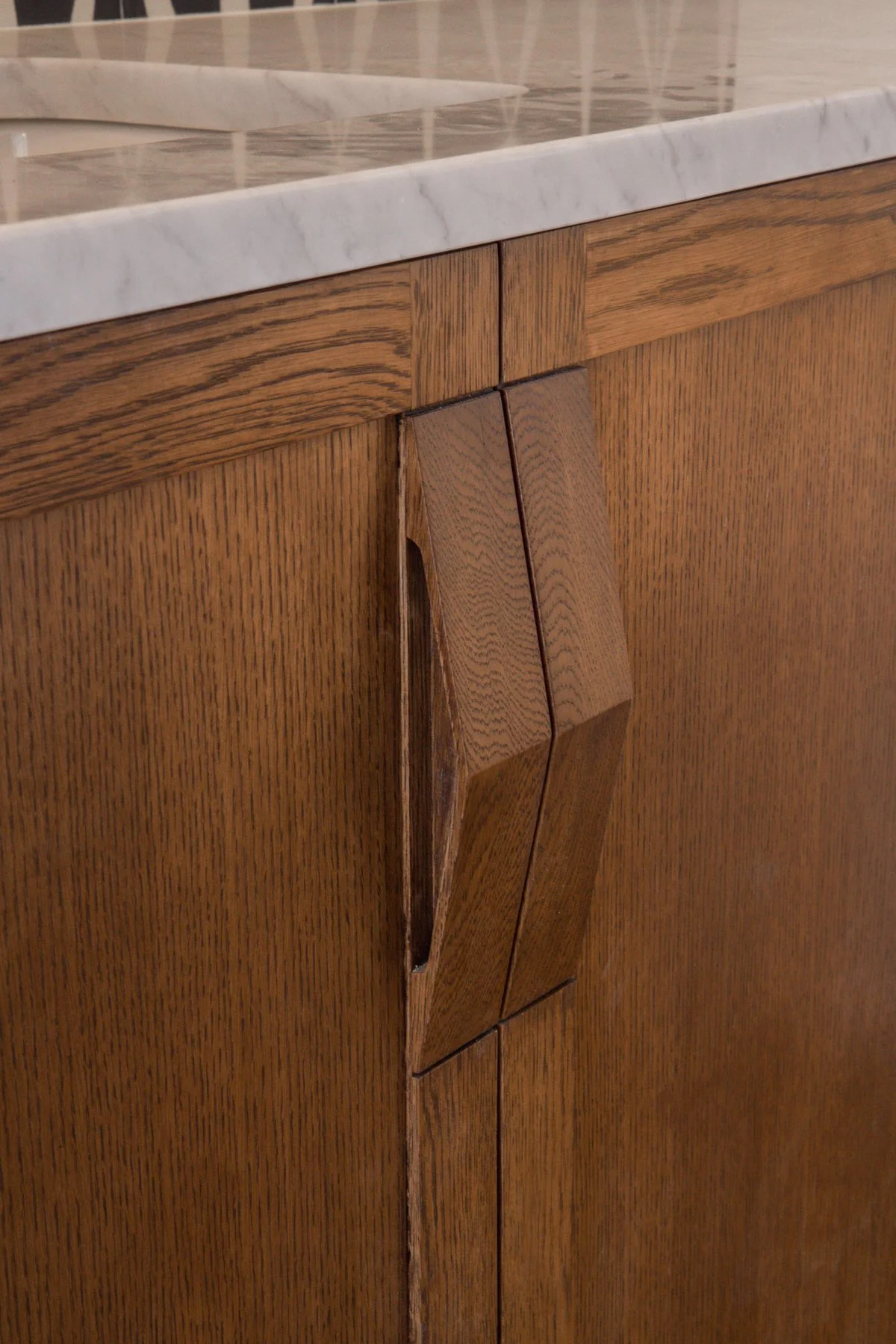 Close-up of a wooden cabinet with a marble countertop, featuring a portion with damaged or unaligned wood panels.  The attention to detail in the wood craftsmanship is very elevated and shares design notes of deco, and mid century design.