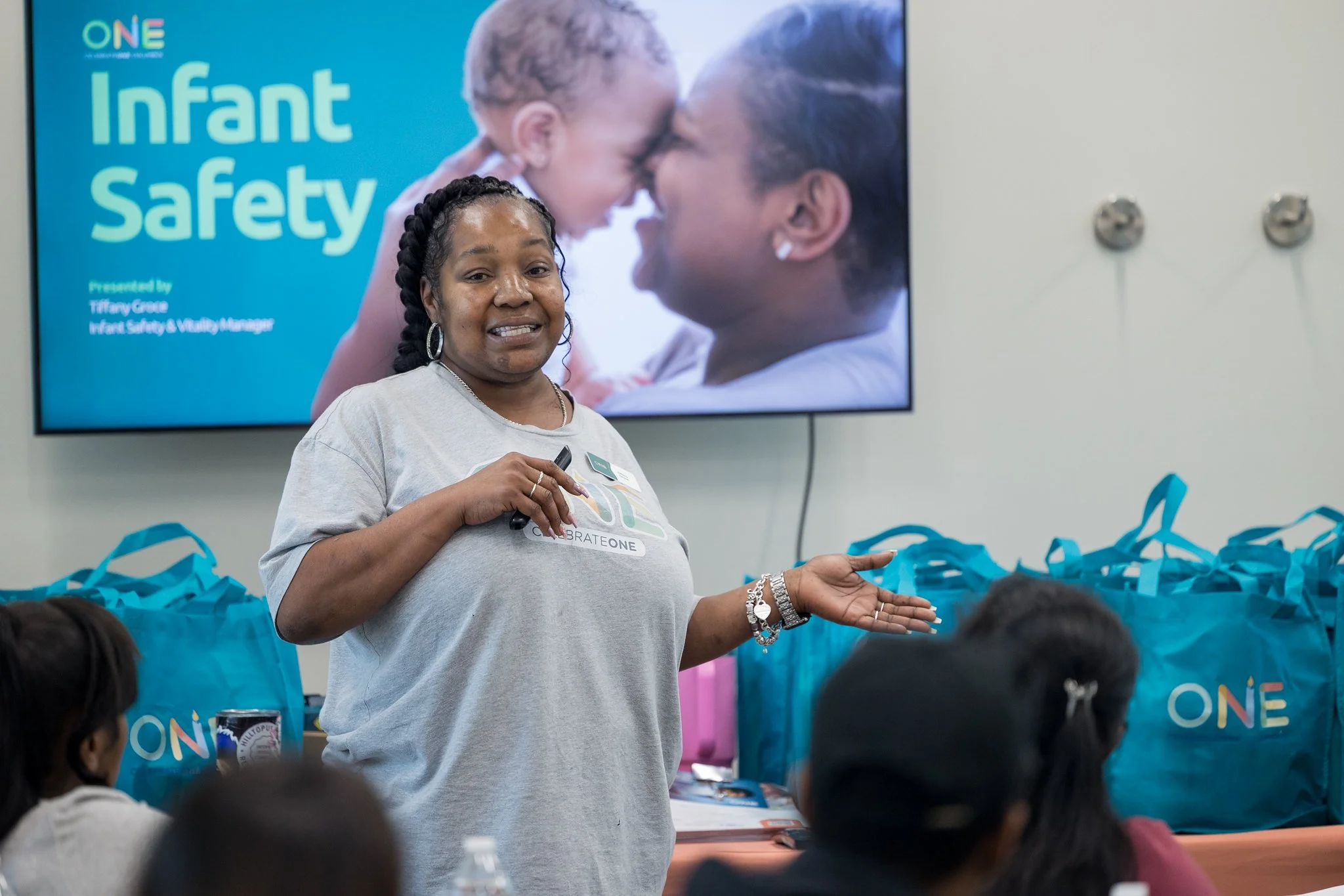CelebrateOne employee in front of a TV screen that says "Infant Safety." She is speaking to a crowd.