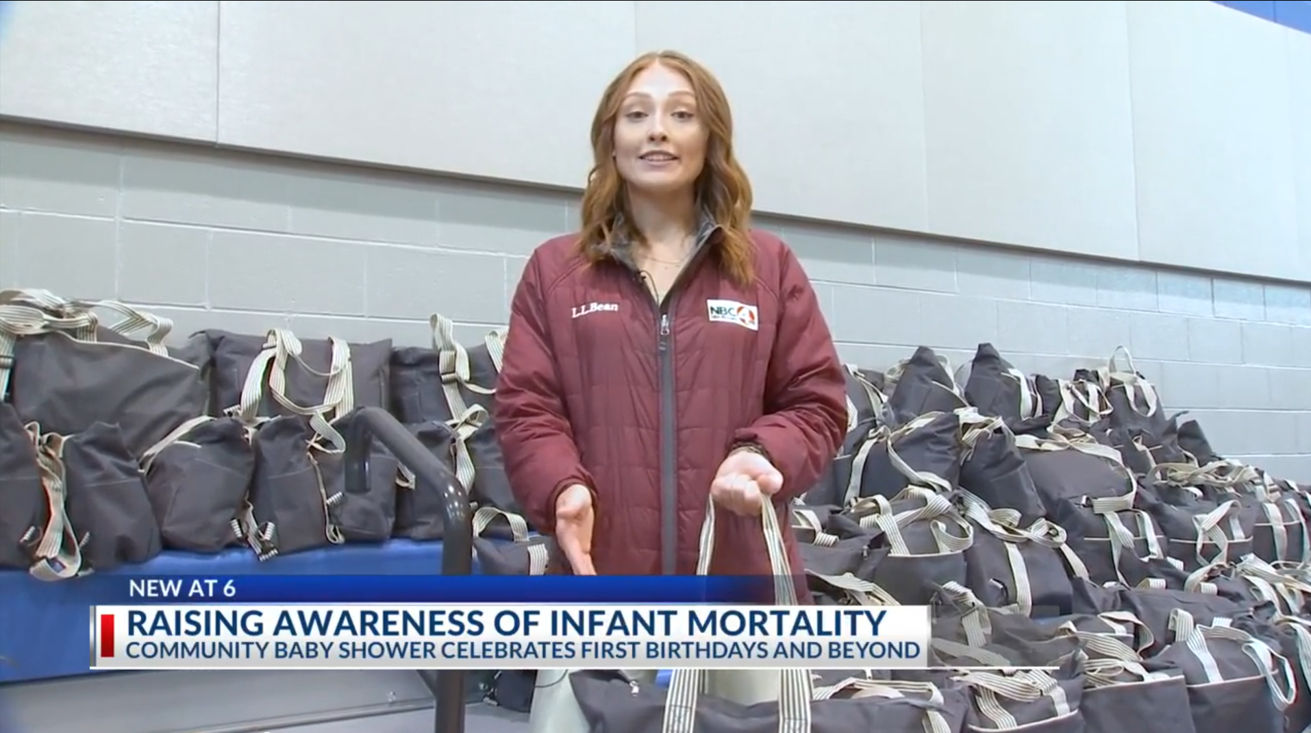News reporter standing in front of a table filled with numerous black bags, participating in a community baby shower event to raise awareness of infant mortality.