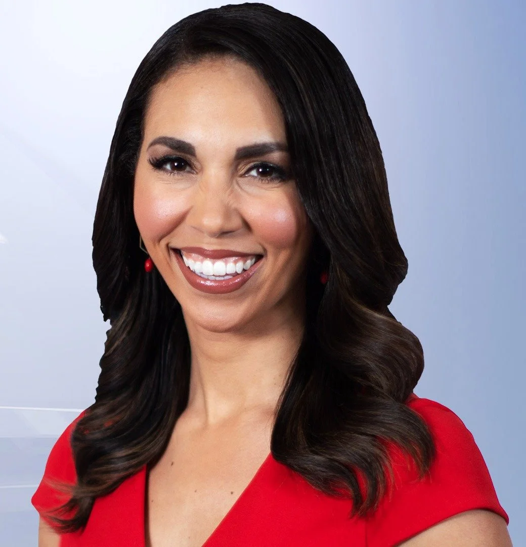 A smiling woman with long dark hair, wearing a red dress and red earrings, posing in front of a neutral background.