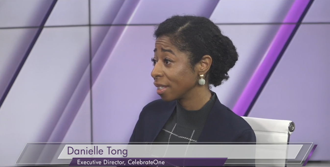 A woman with curly black hair sitting and speaking in a TV studio, with a purple and gray background. She is wearing a black blazer and earrings. The lower third label reads "Danielle Tong, Executive Director, CelebrateOne."