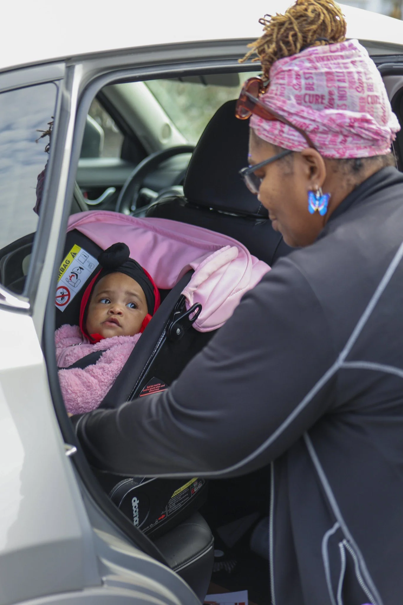 CelebrateOne employee leans into back car door looking down on a baby in a car seat.