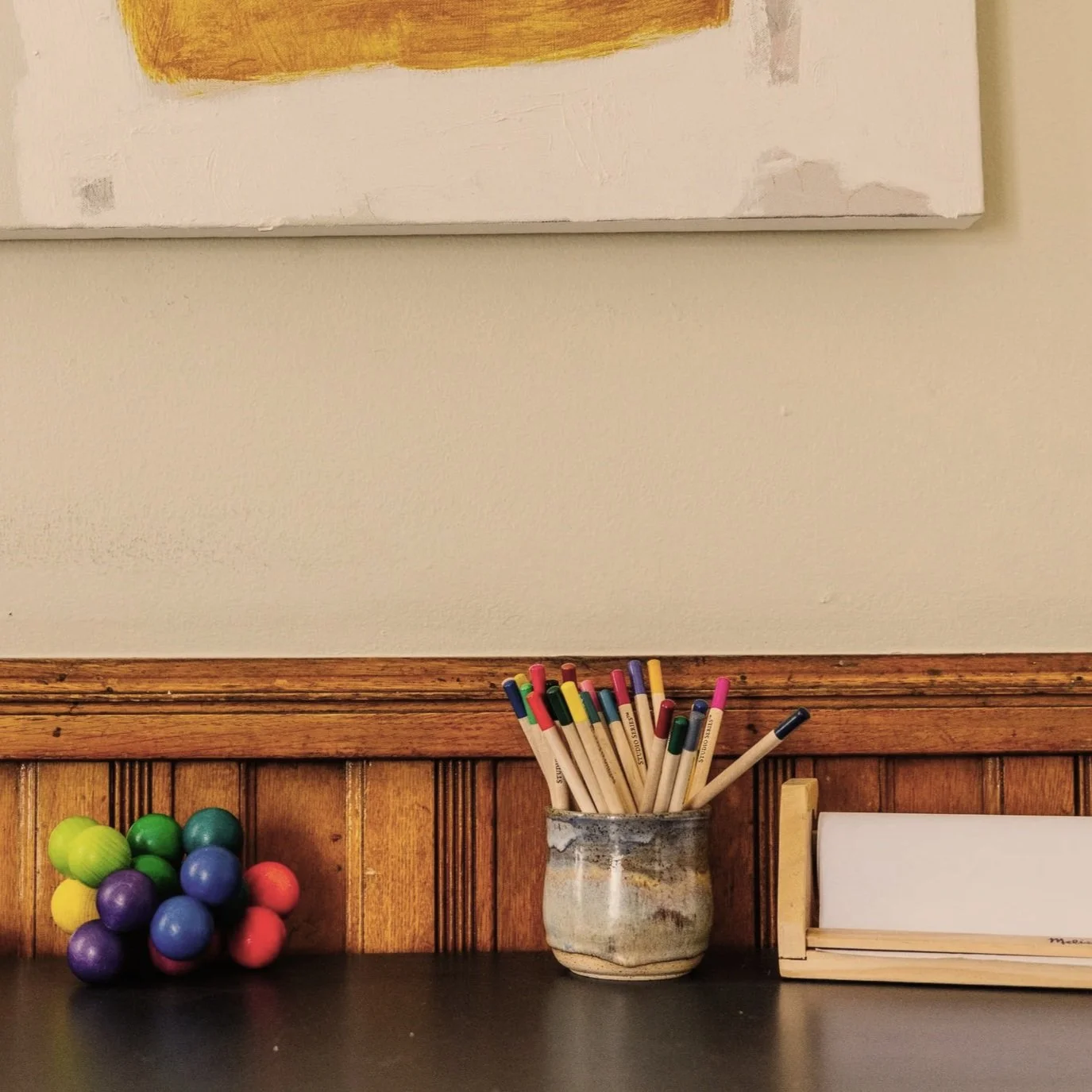 Colorful markers in a wooden holder, with a blurred hand holding a marker in the background.