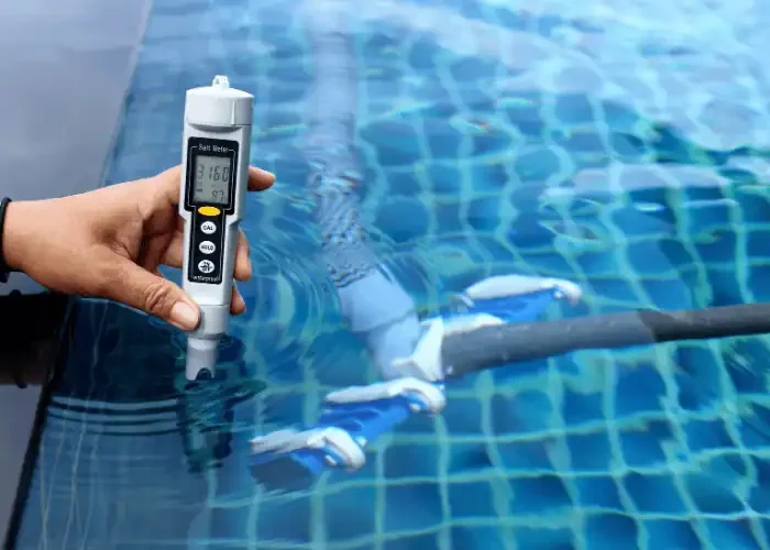 Hand holding digital water quality meter measuring pool water pH or chemical levels.