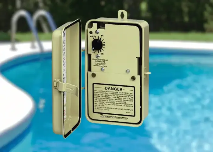 An electrical control box mounted on a white pole near a swimming pool with blue water, greenery in the background, and a ladder.