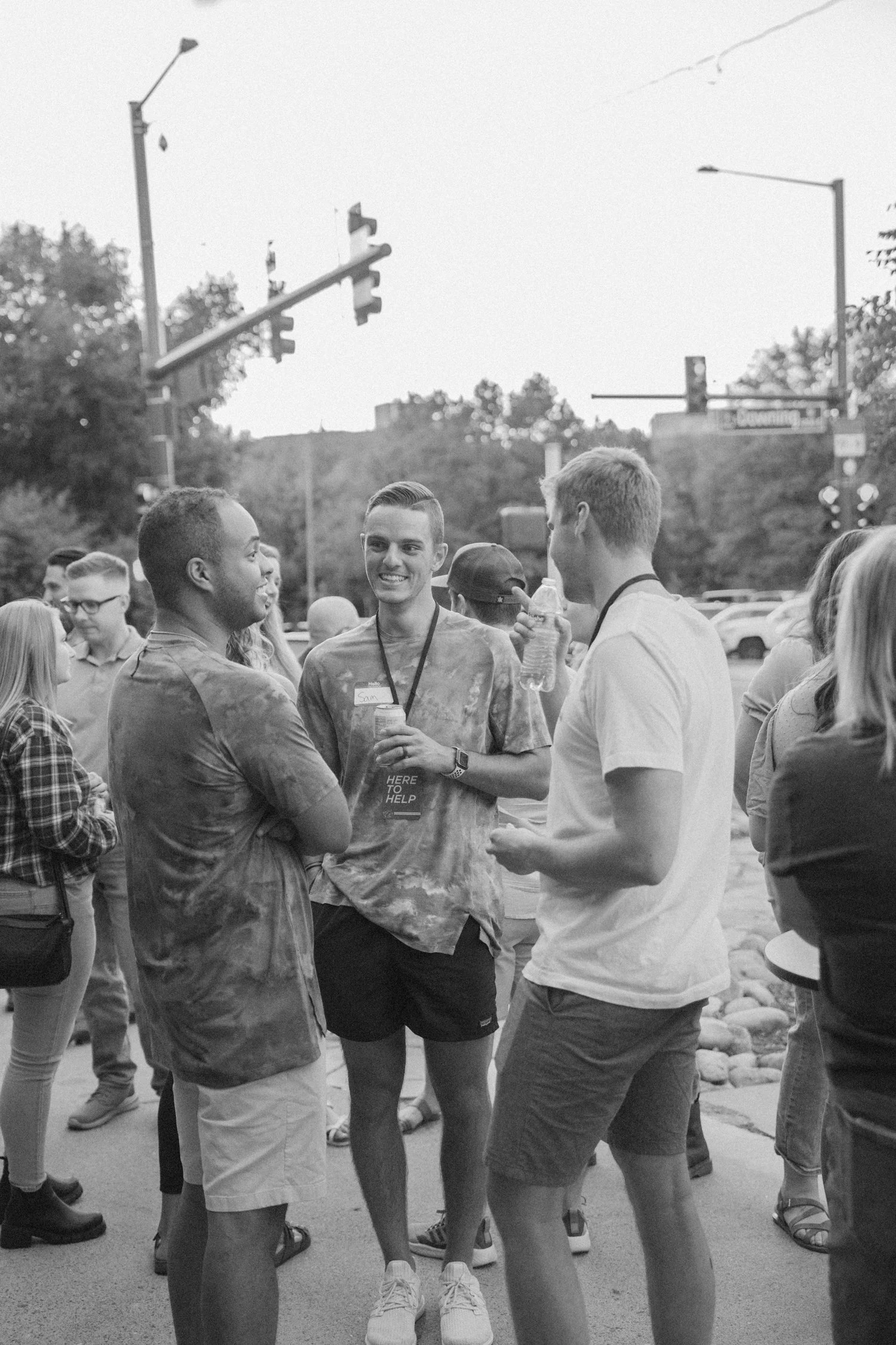 Group of young adults socializing outdoors during daytime at a gathering or event, engaged in conversation, some holding drinks.