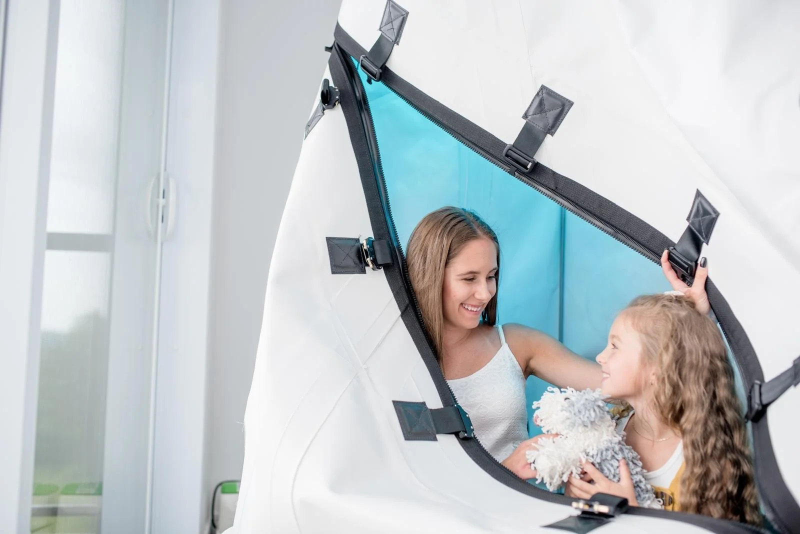 Une femme et une jeune fille avec un chien à l'intérieur d'une tente de photographie portative. La femme sourit et regarde la jeune fille, qui tient un chien blanc, gris et beige.