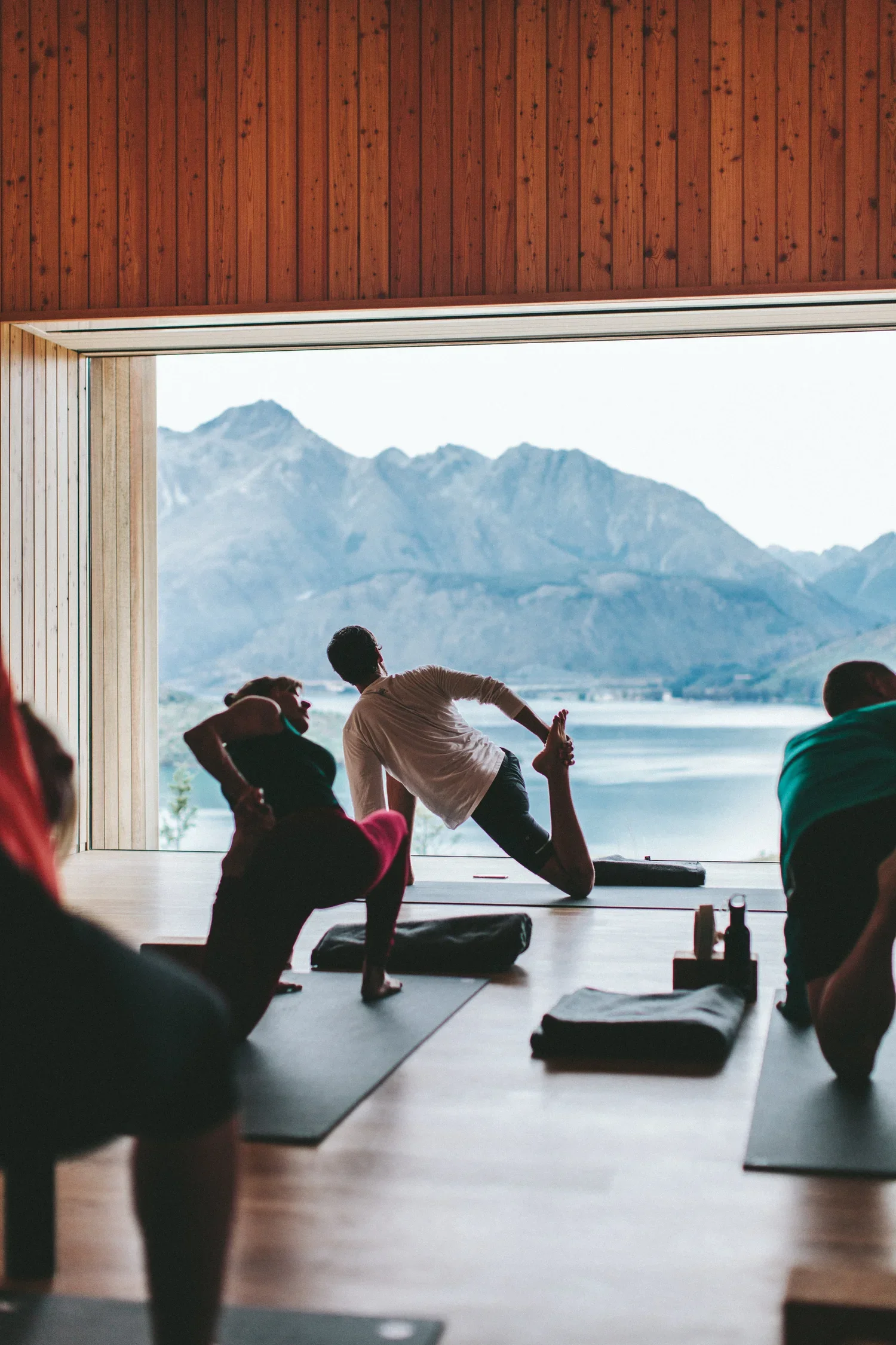 Groupe de personnes pratiquant le yoga dans une salle avec vue sur des montagnes et un lac.