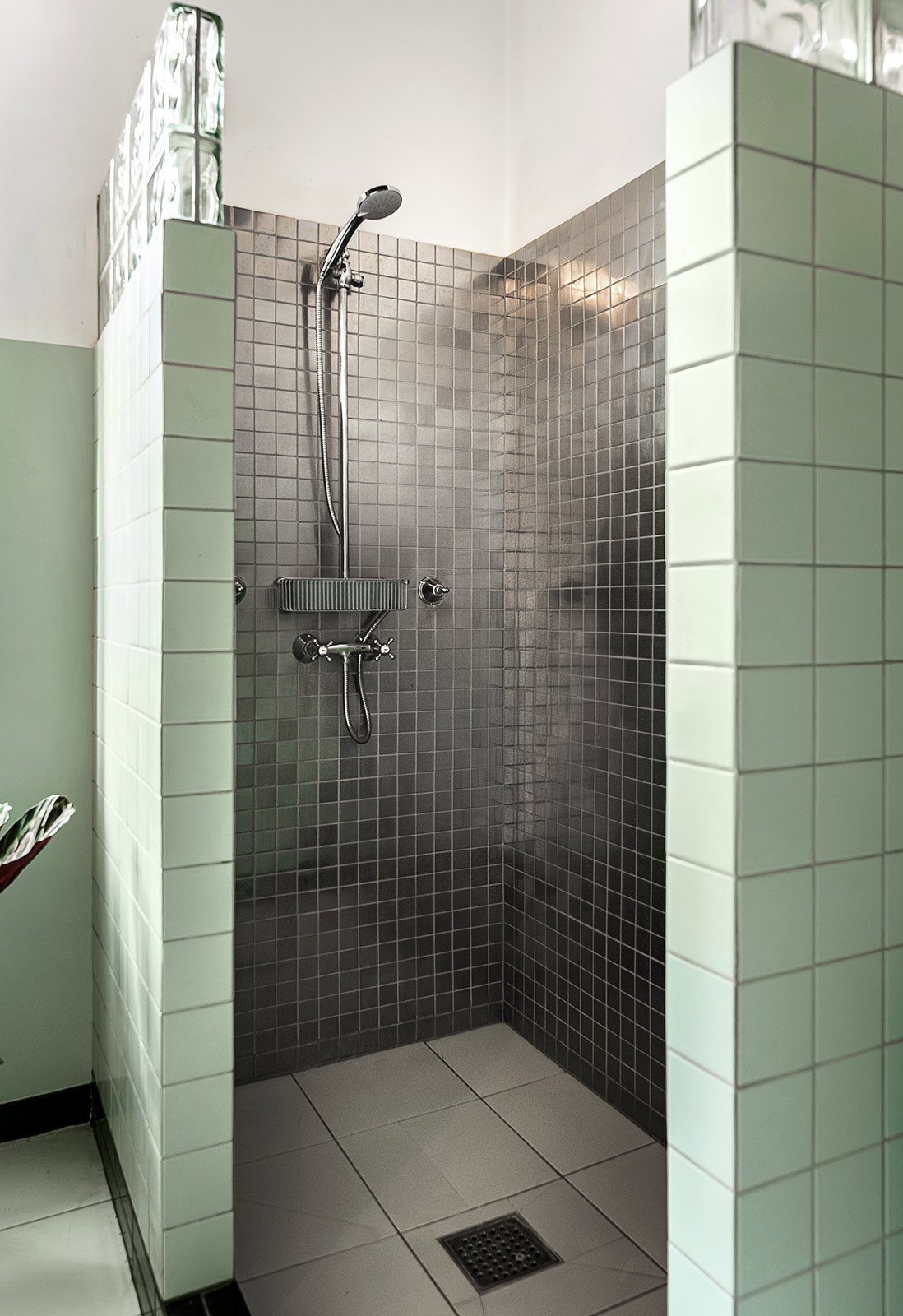 Empty shower stall with dark gray tiles, a handheld showerhead, and a small shelf, surrounded by white tiled walls.