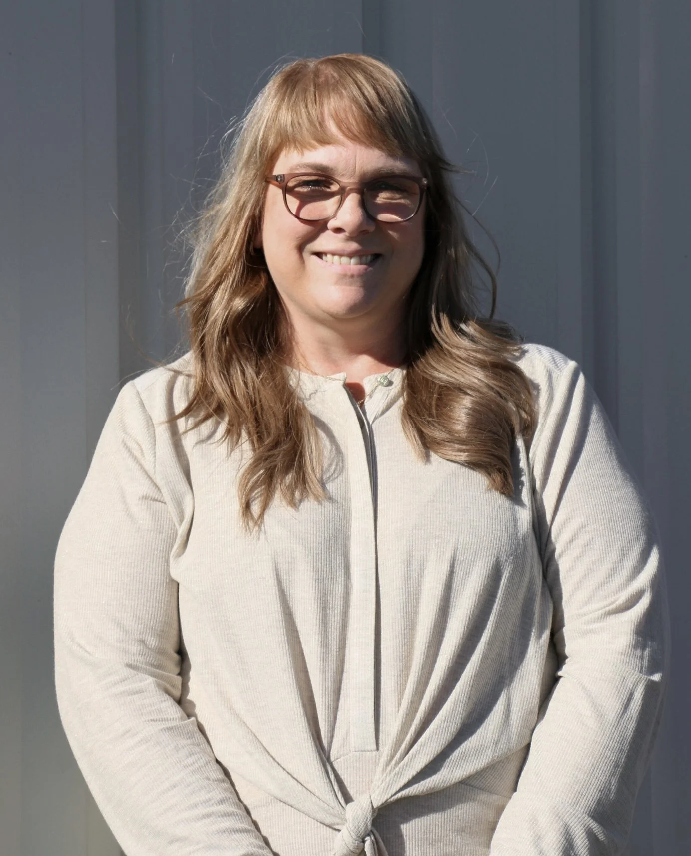 A woman with long gray hair, glasses, and a floral dress smiling at the camera.