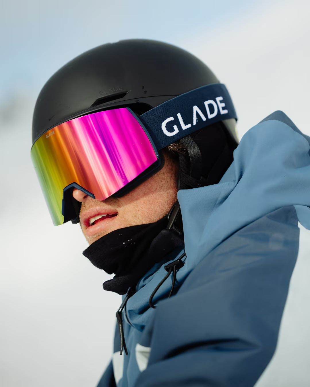Close-up of a person wearing a black helmet and colorful goggles, dressed in a blue winter jacket, likely engaging in a winter sport.
