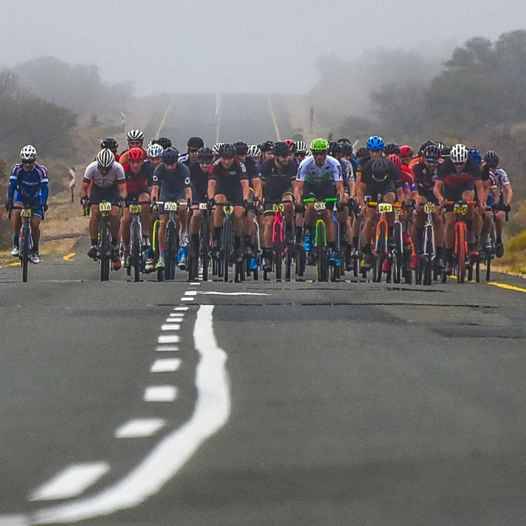 A large group of cyclists riding on a foggy road, wearing brightly colored helmets and jerseys.