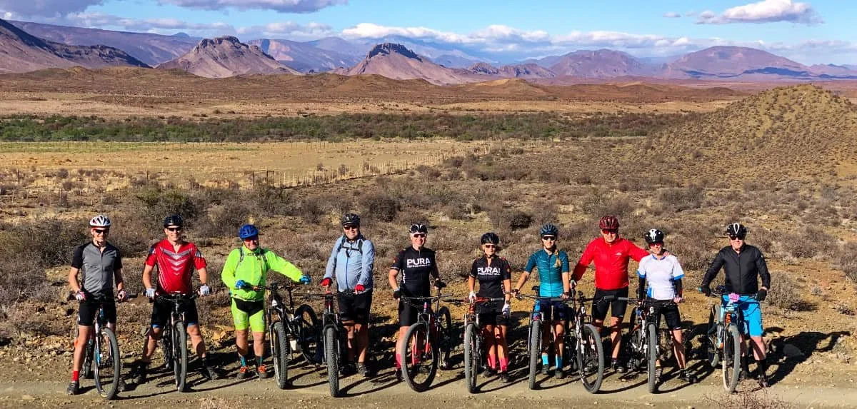 Group of ten people with bicycles standing in a desert landscape with mountains in the background.