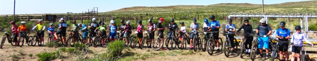 Group of children and teens with bicycles, wearing helmets, standing in a row outdoors.