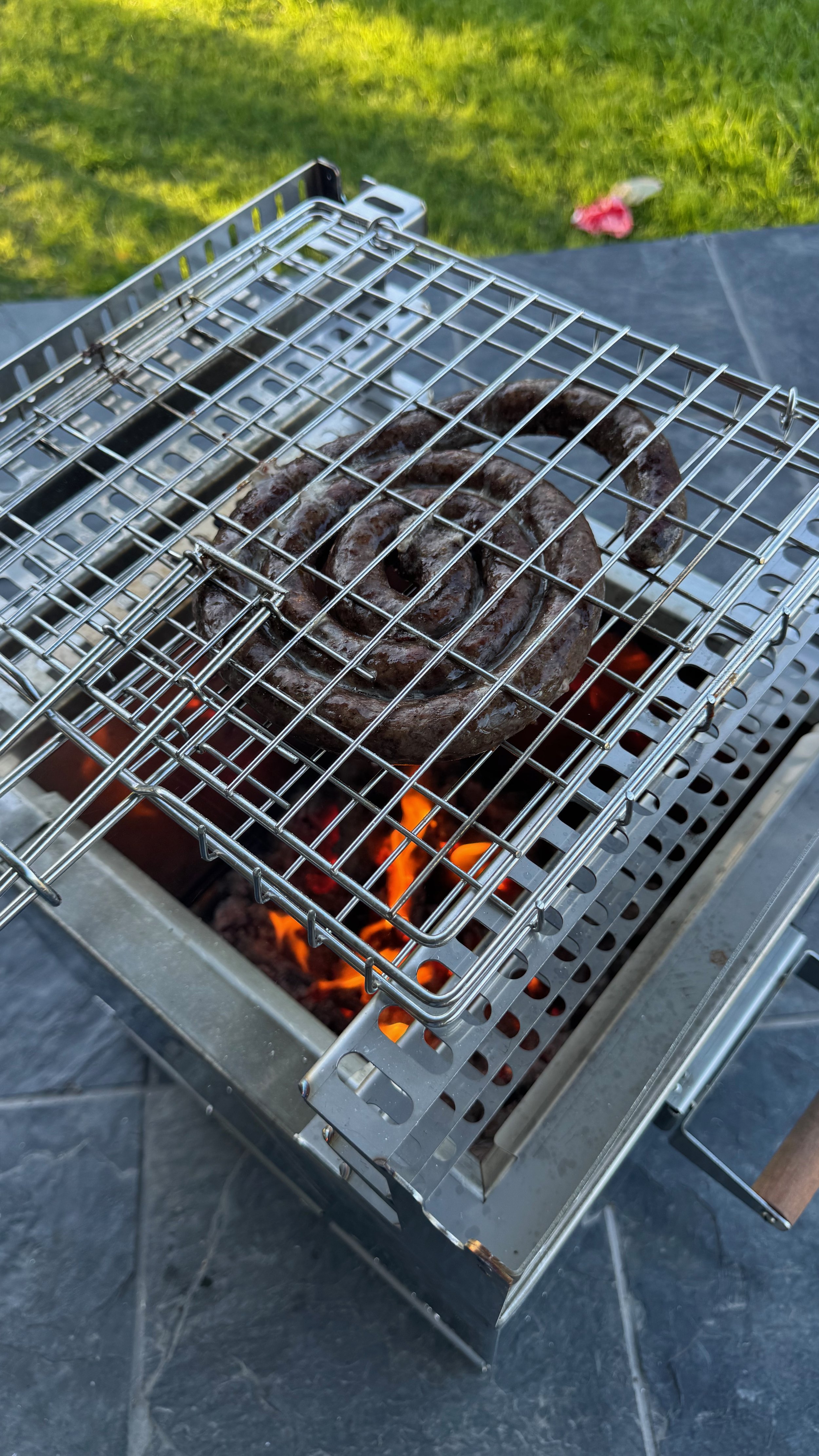 Sausage links cooking on a grill over open flame.