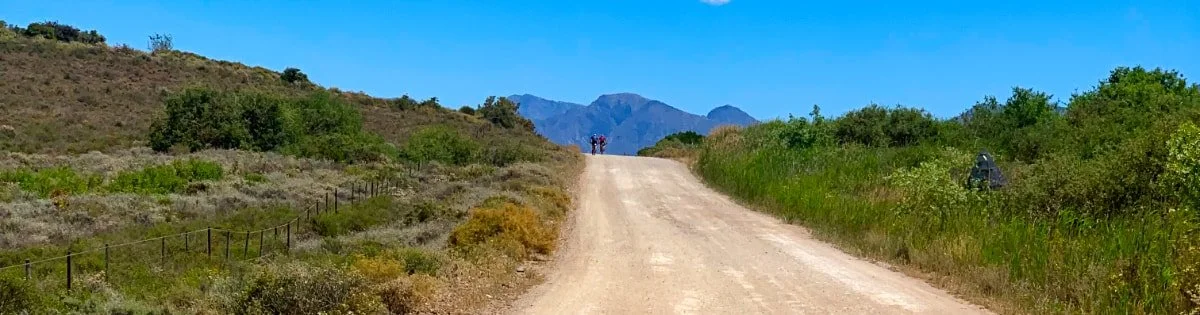 A dirt road running through a hilly landscape with mountains in the background and a clear blue sky.