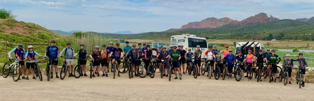 Group of people with bicycles on a dirt trail with mountains in the background.