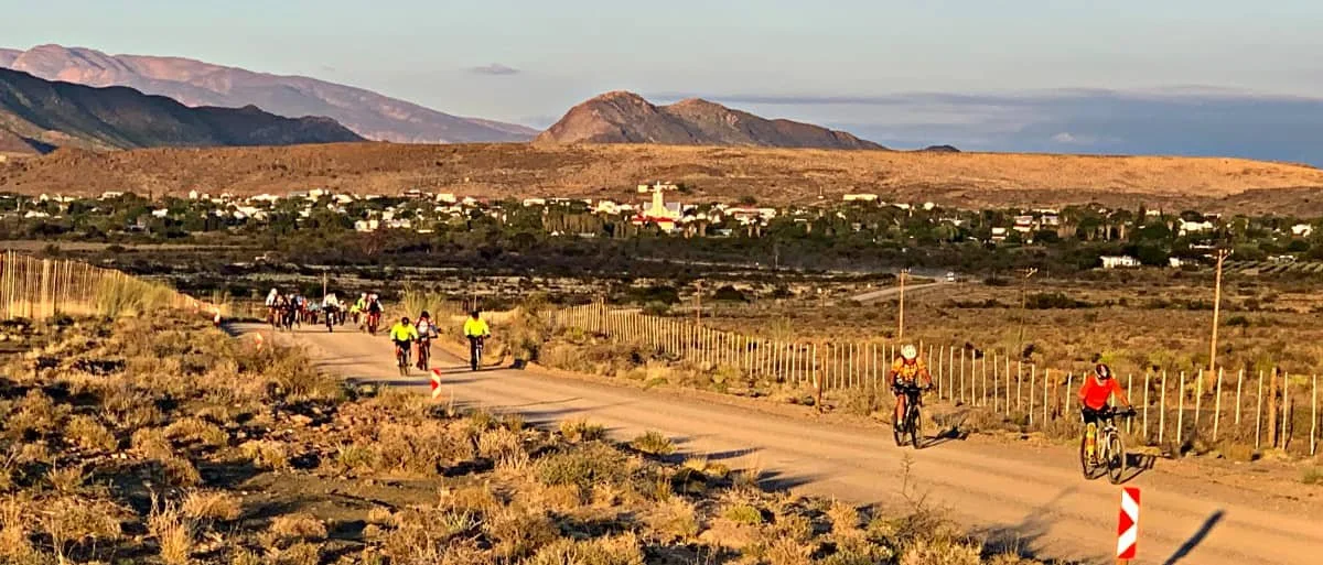 Group of people cycling on a dirt road through a desert landscape with mountains in the background.