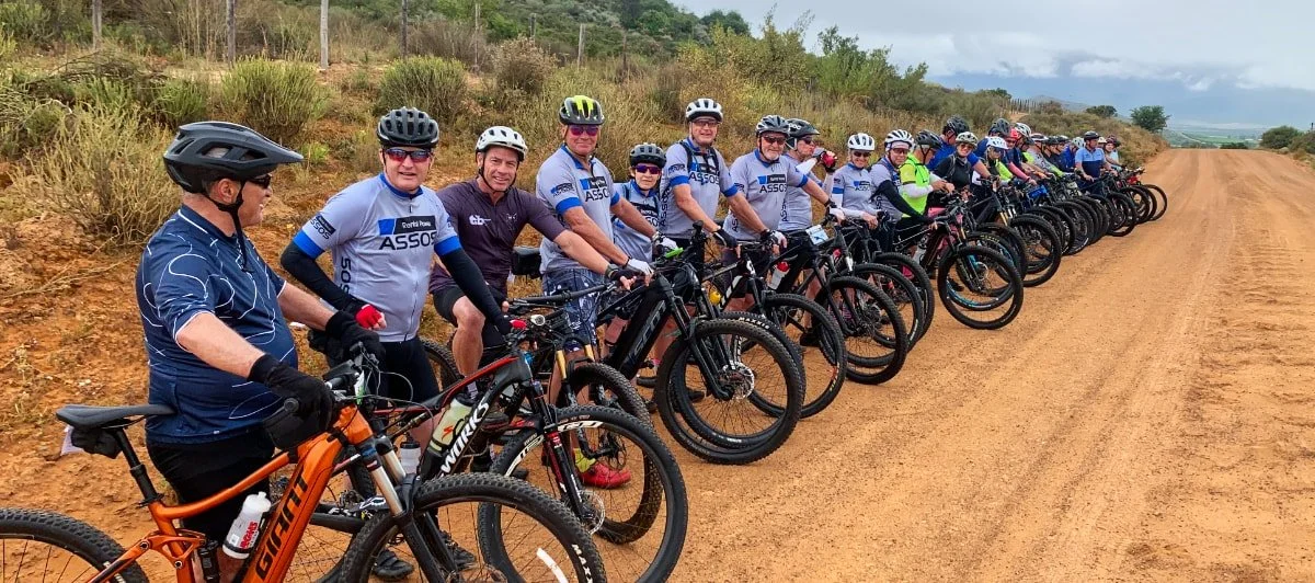 Group of cyclists wearing helmets and riding bikes on a dirt road in a rural area.