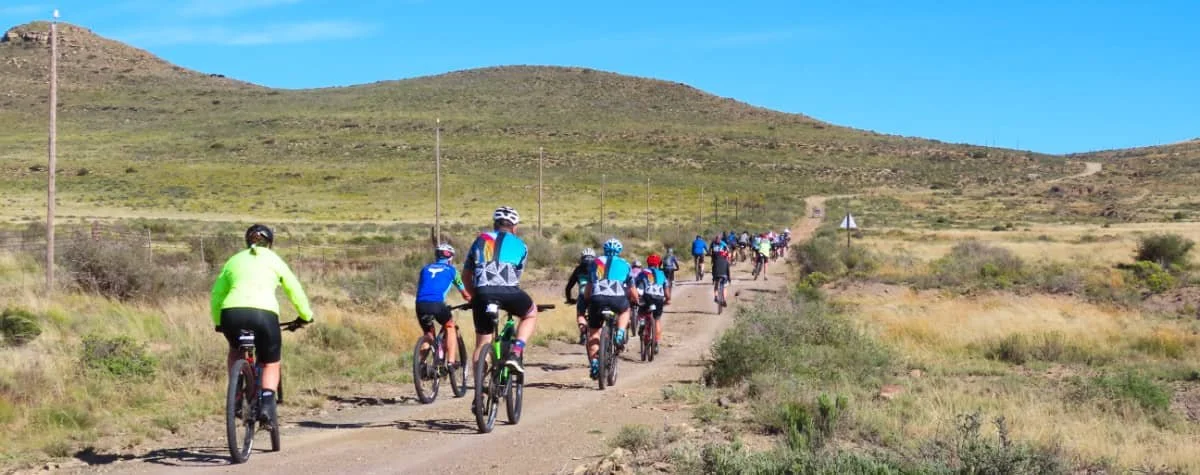 A group of cyclists riding on a dirt trail in a hilly, grassy landscape with clear blue skies.