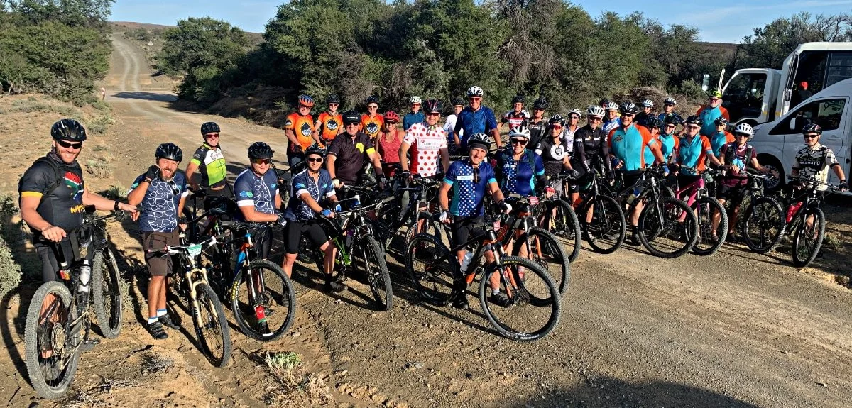 Group of people with bicycles posing for a photo on a dirt trail in a rural area.