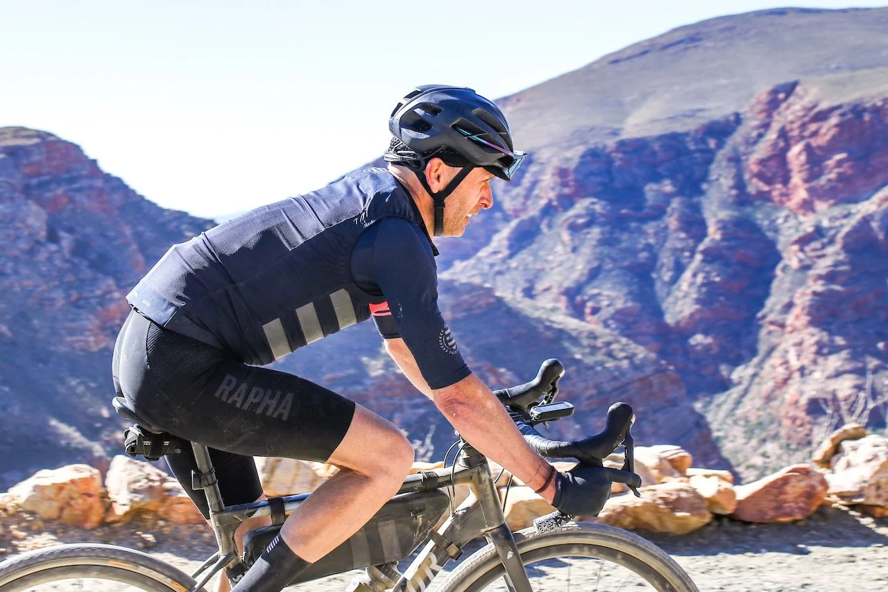 A man riding a bicycle in a mountainous area with rocky terrain and clear blue sky.