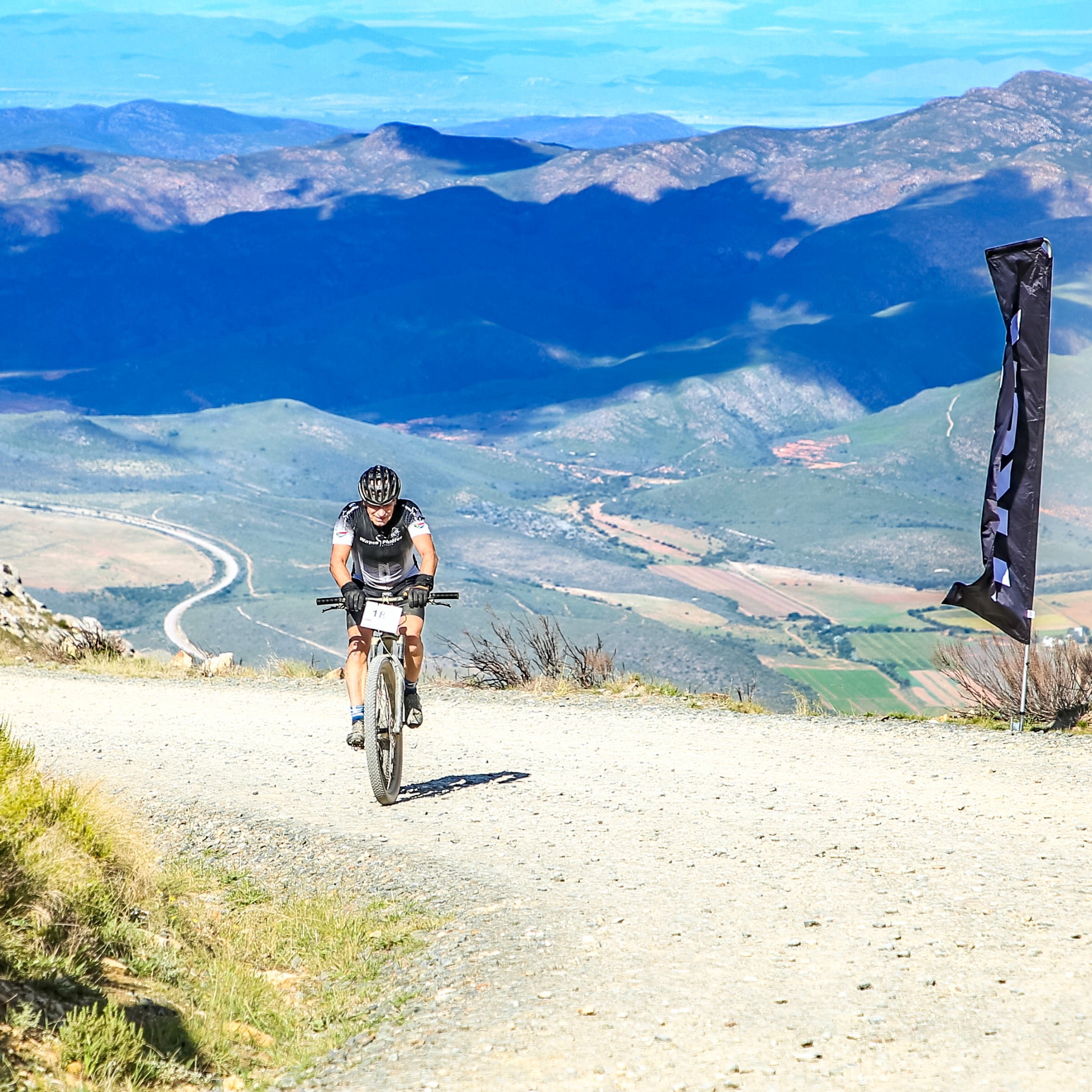 A cyclist riding on a dirt trail on a mountain with scenic landscape and valleys in the background.