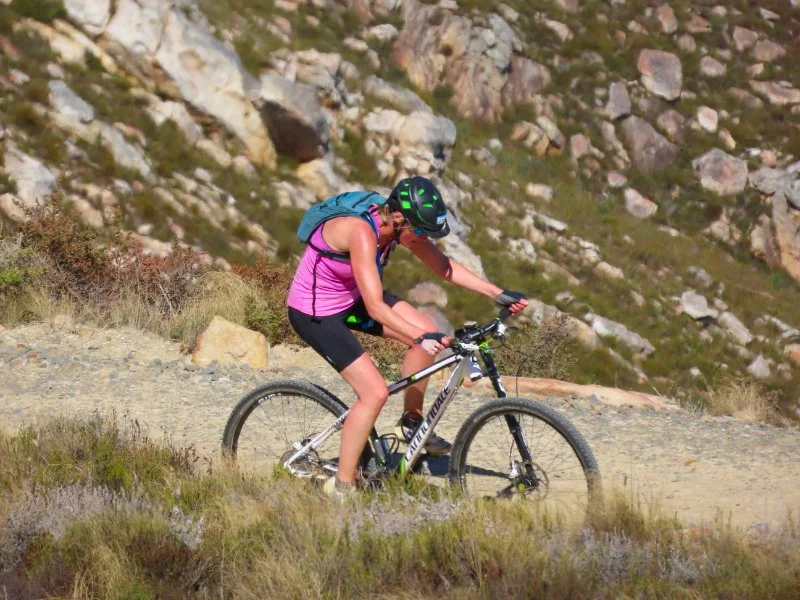 A person mountain biking on a trail in a rocky, mountainous area with sparse vegetation.