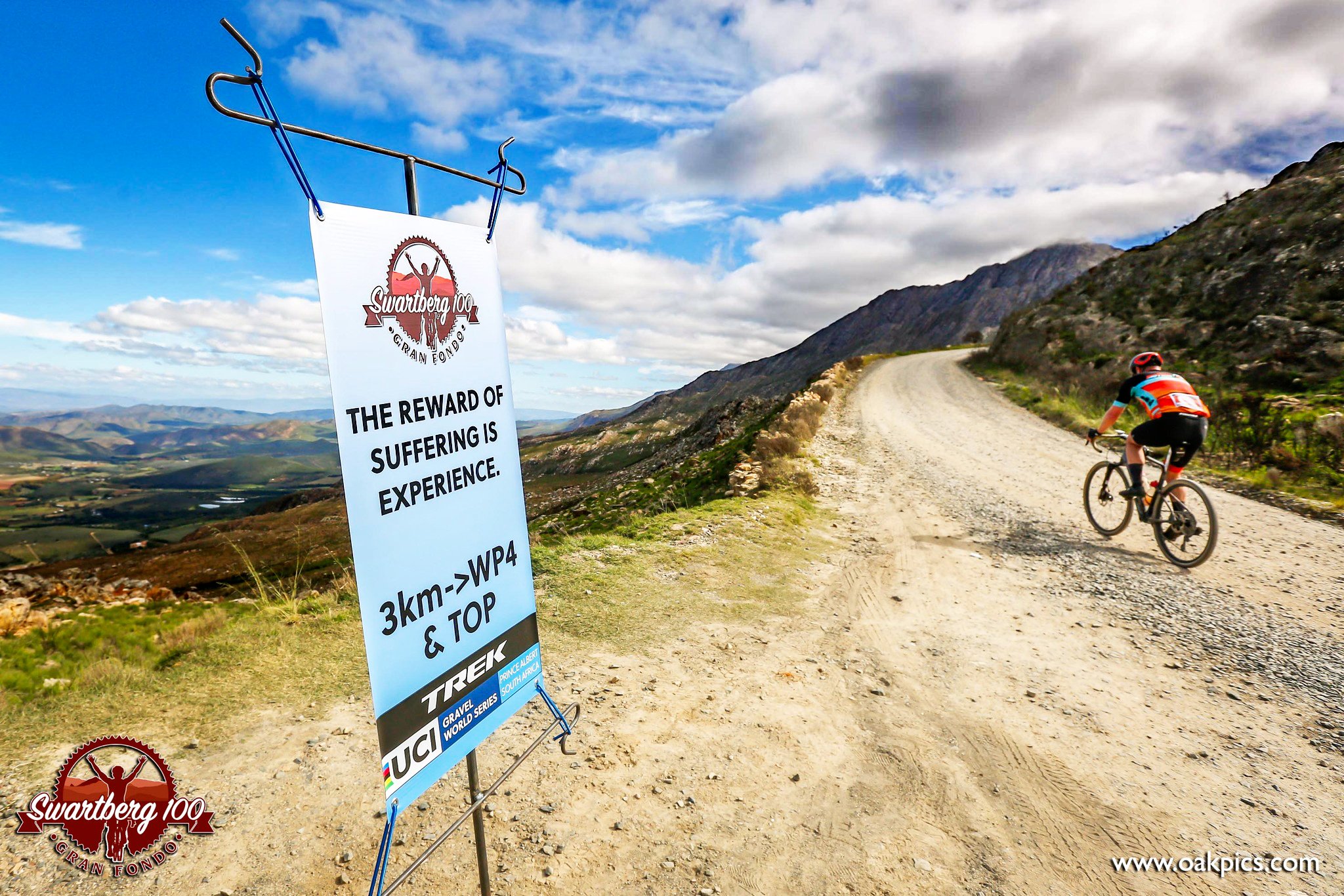 Cyclist riding on a dirt mountain road with a sign that says "The reward of suffering is experience" and logos for Swartberg 100 and UCI Gravel World Series.