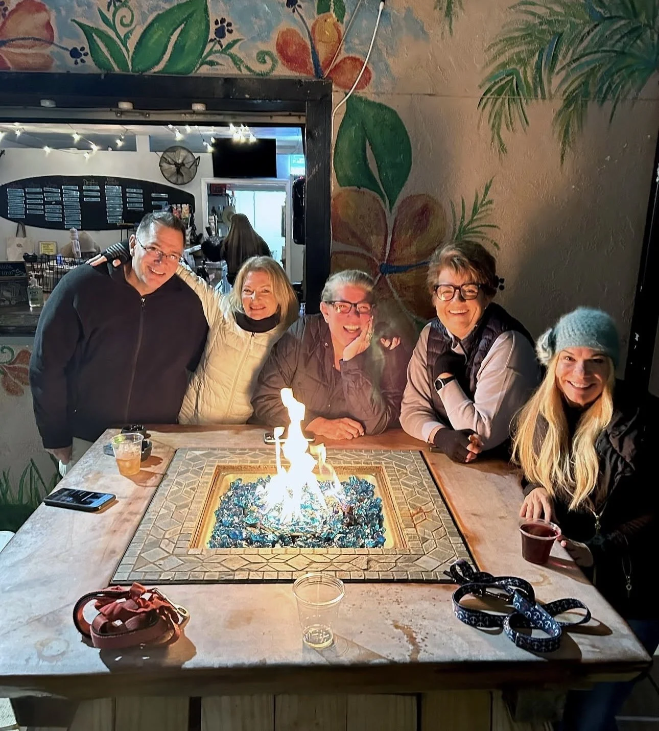 Group of five friends celebrating a birthday around a table with a cake that has sparklers, in a restaurant with colorful wall art.