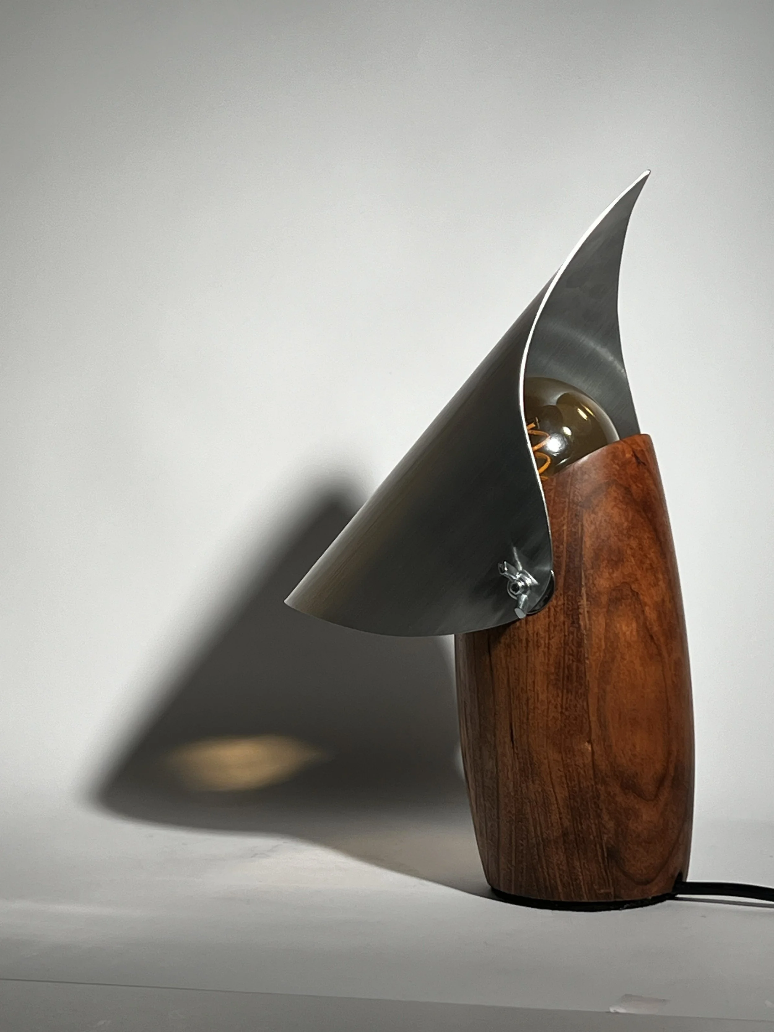 Desk lamp with a wooden base, metallic shade, and exposed light bulb, casting a shadow on a plain white background.