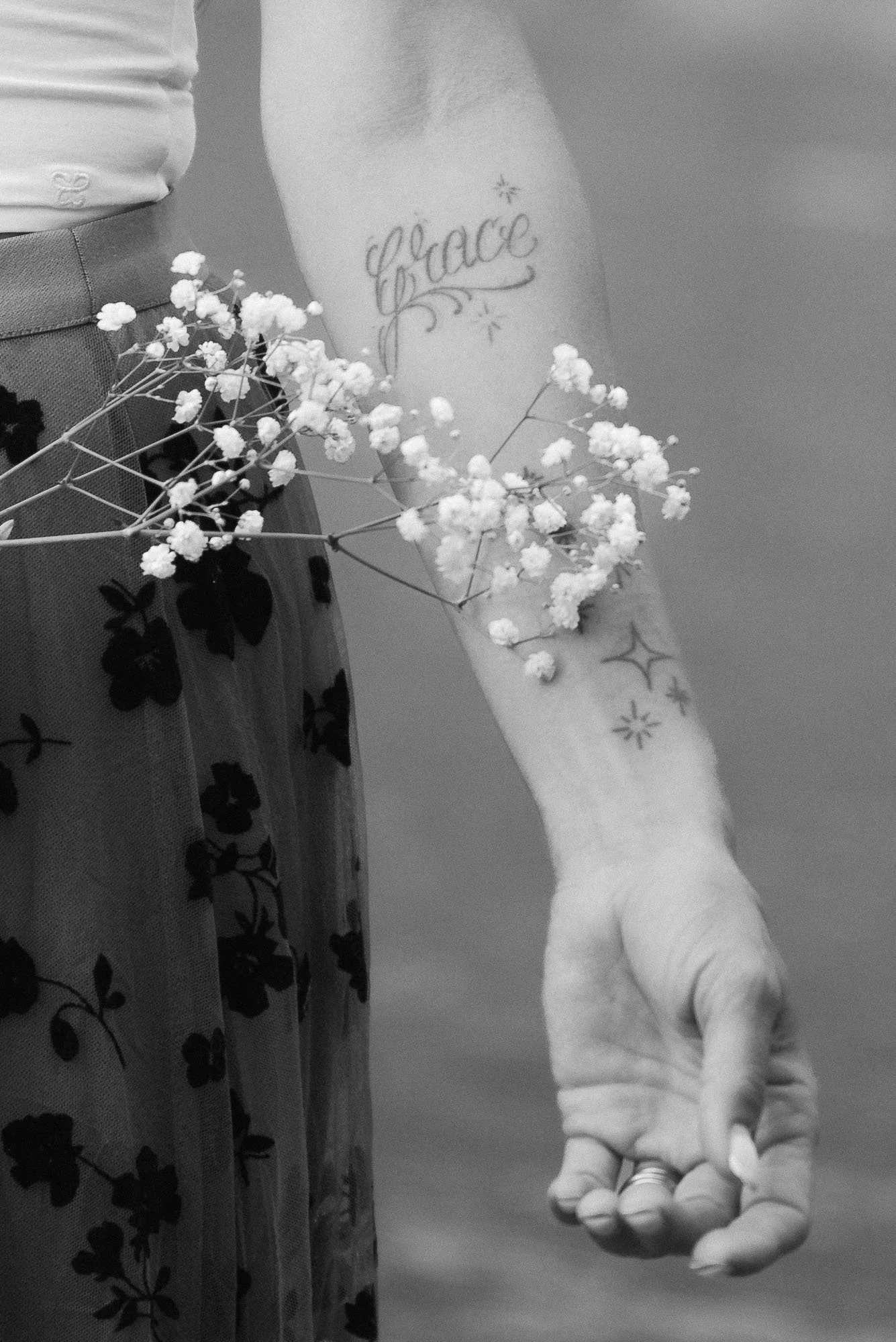 A person's arm with tattoos and a dress, holding a small bouquet of white baby's breath flowers.