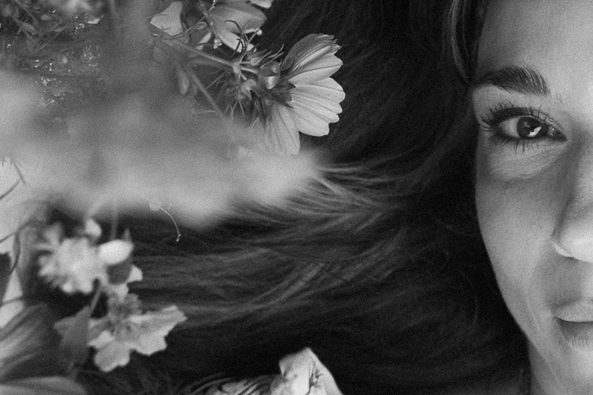 Close-up of a fertility coach in Edmonton Justine Lapointe's face, showing her right eye, smile, and flowing hair, with flowers and plants in the background, all in black and white.