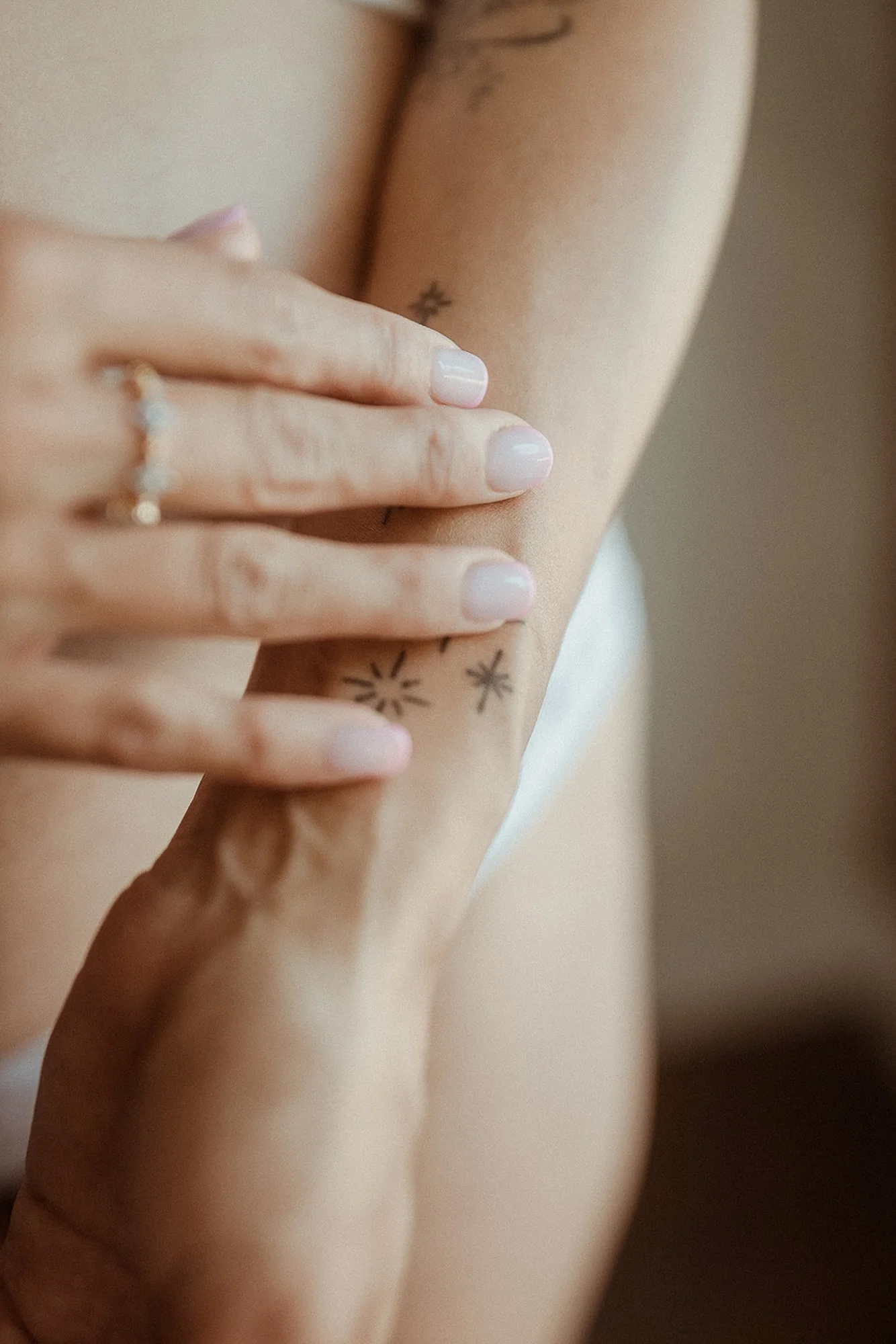 Close-up of a woman's arm with tattoos, her hand resting on her arm, displaying manicured nails and a ring.