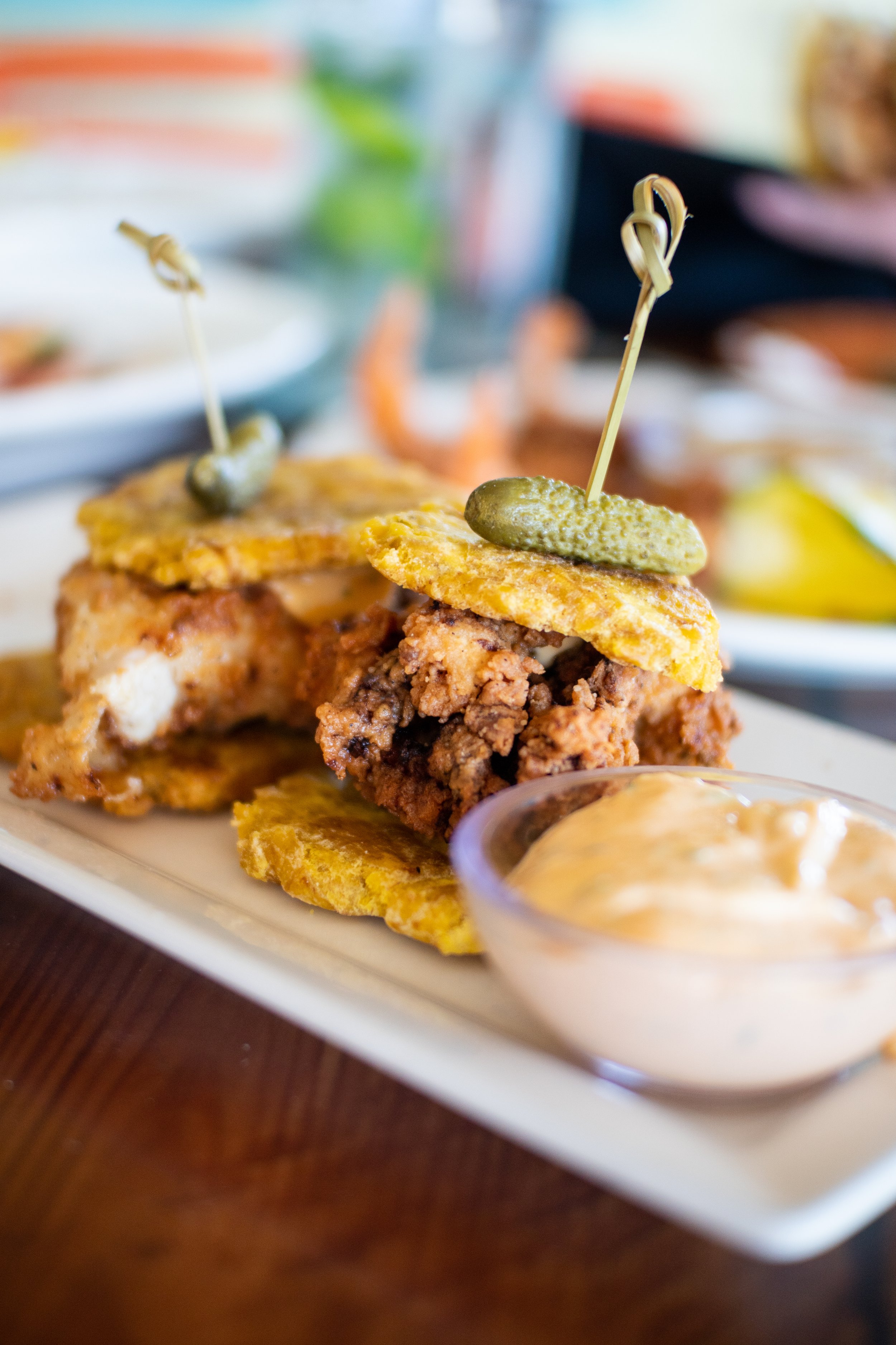 Fried chicken with pickle-topped waffle sliders served with dipping sauce on a white platter.