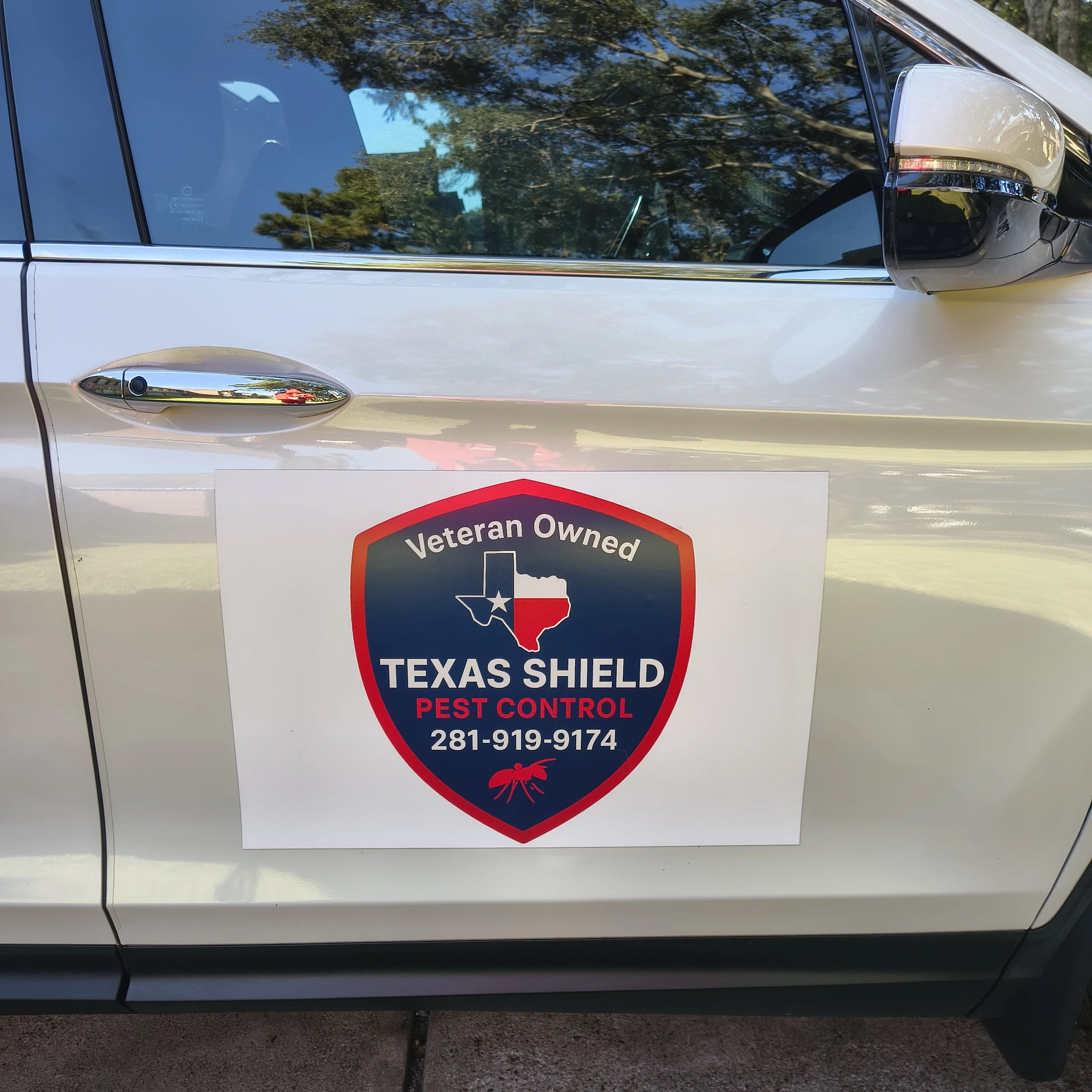 Vehicle with a Texas Shield Pest Control decal. The decal is shield-shaped, featuring a Texas map with the Texas flag inside it, and text reading 'Veteran Owned Texas Shield Pest Control' along with a phone number.