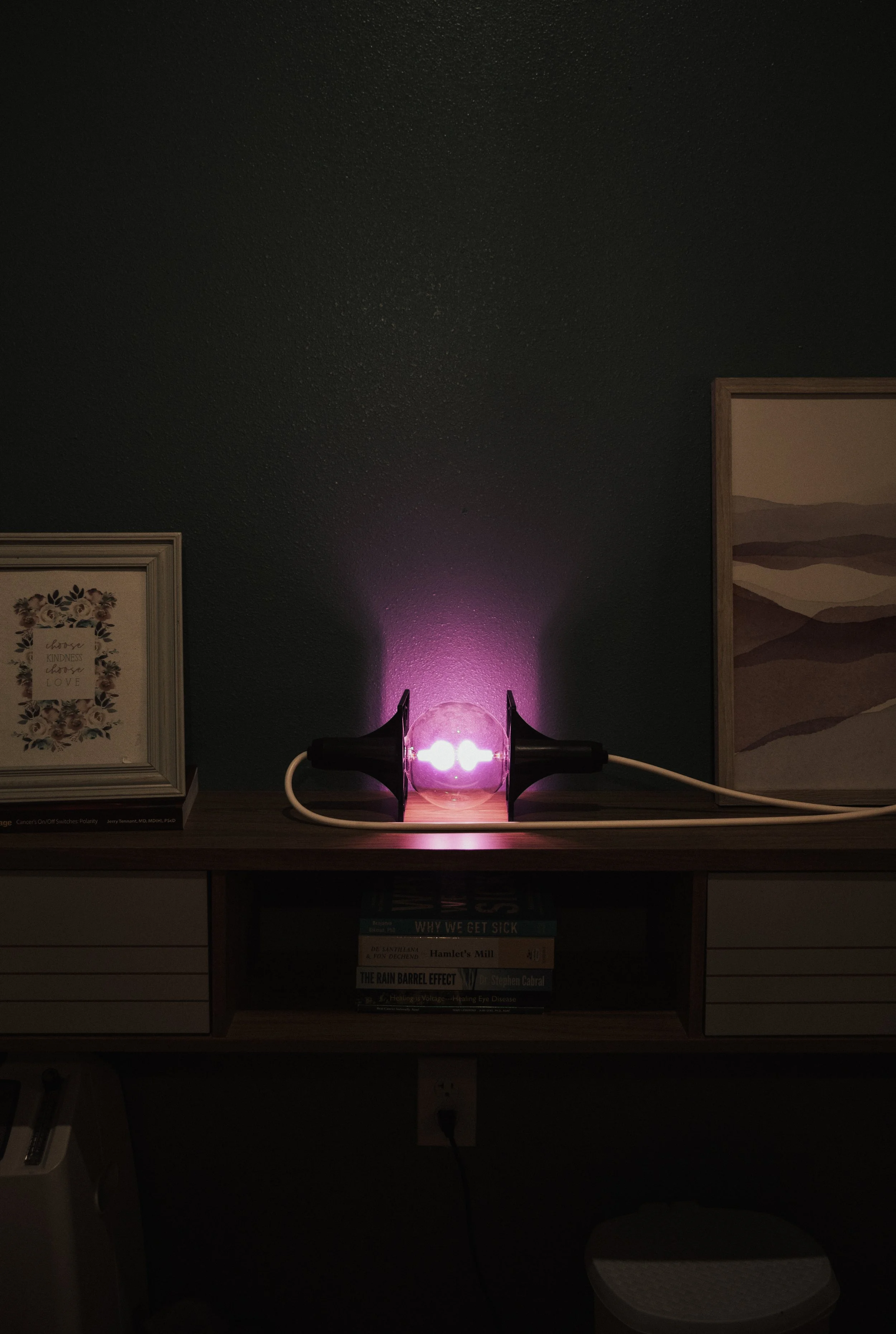 A clear glass sphere with a light inside it, emitting purple light, flanked by two black conical objects, on a wooden surface against a dark wall.