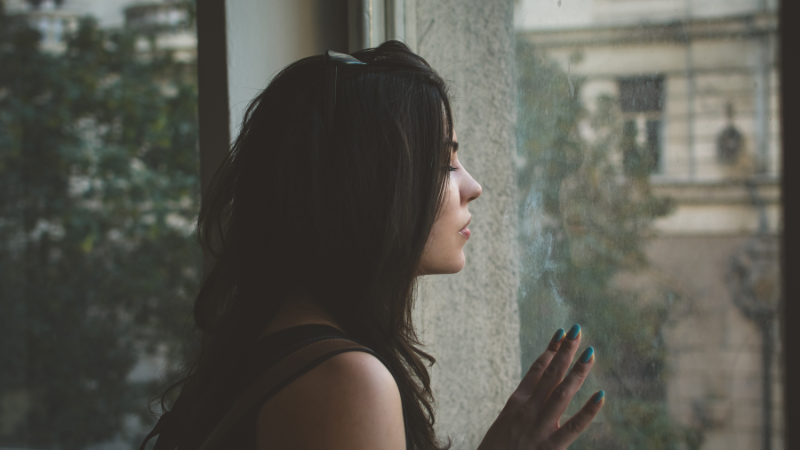 Person gazing through a window symbolizing self-reflection, emotional wellbeing, personal growth, life transitions, and taking the first step toward somatic coaching support.