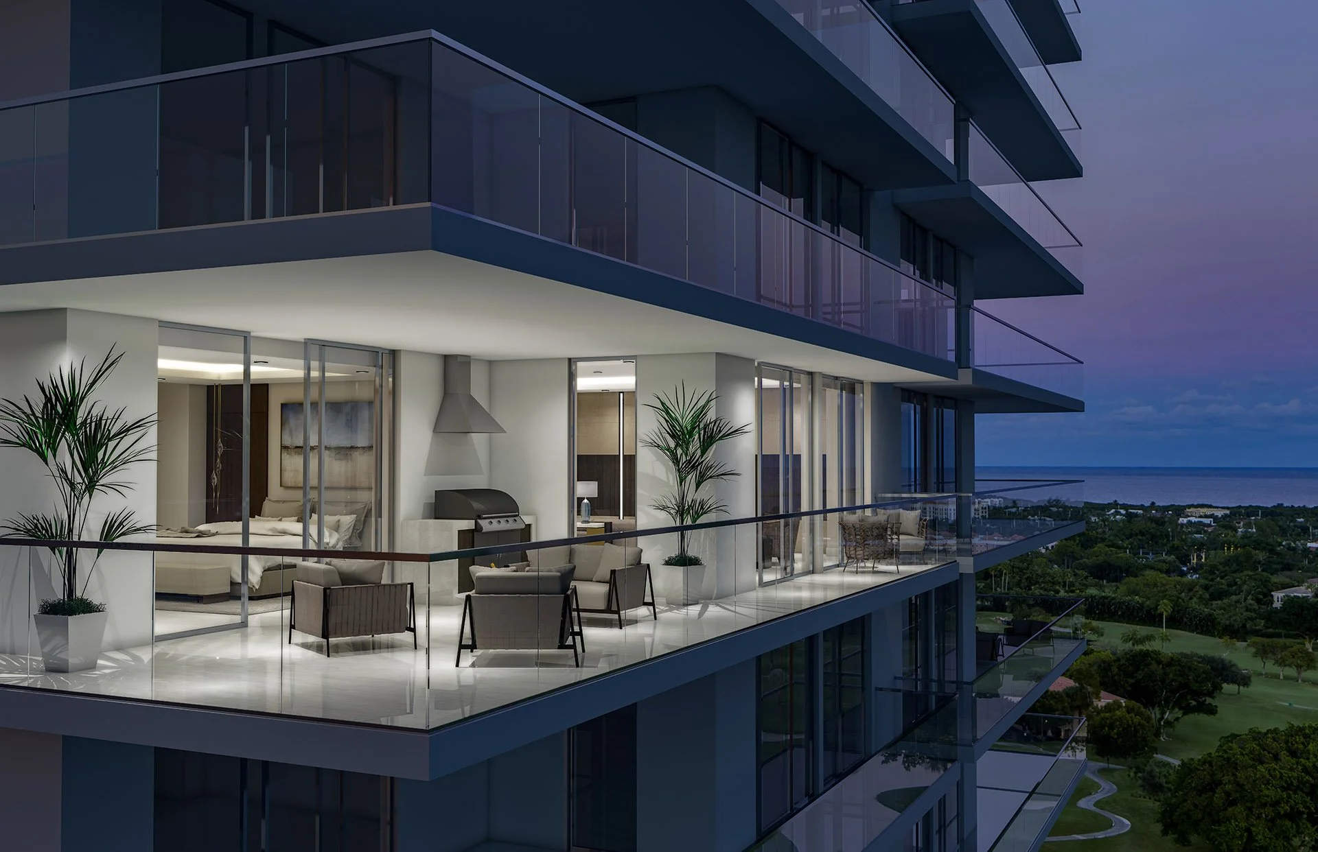 Modern apartment balcony at dusk with outdoor living space, potted plants, chairs, and view of trees and water in the distance.
